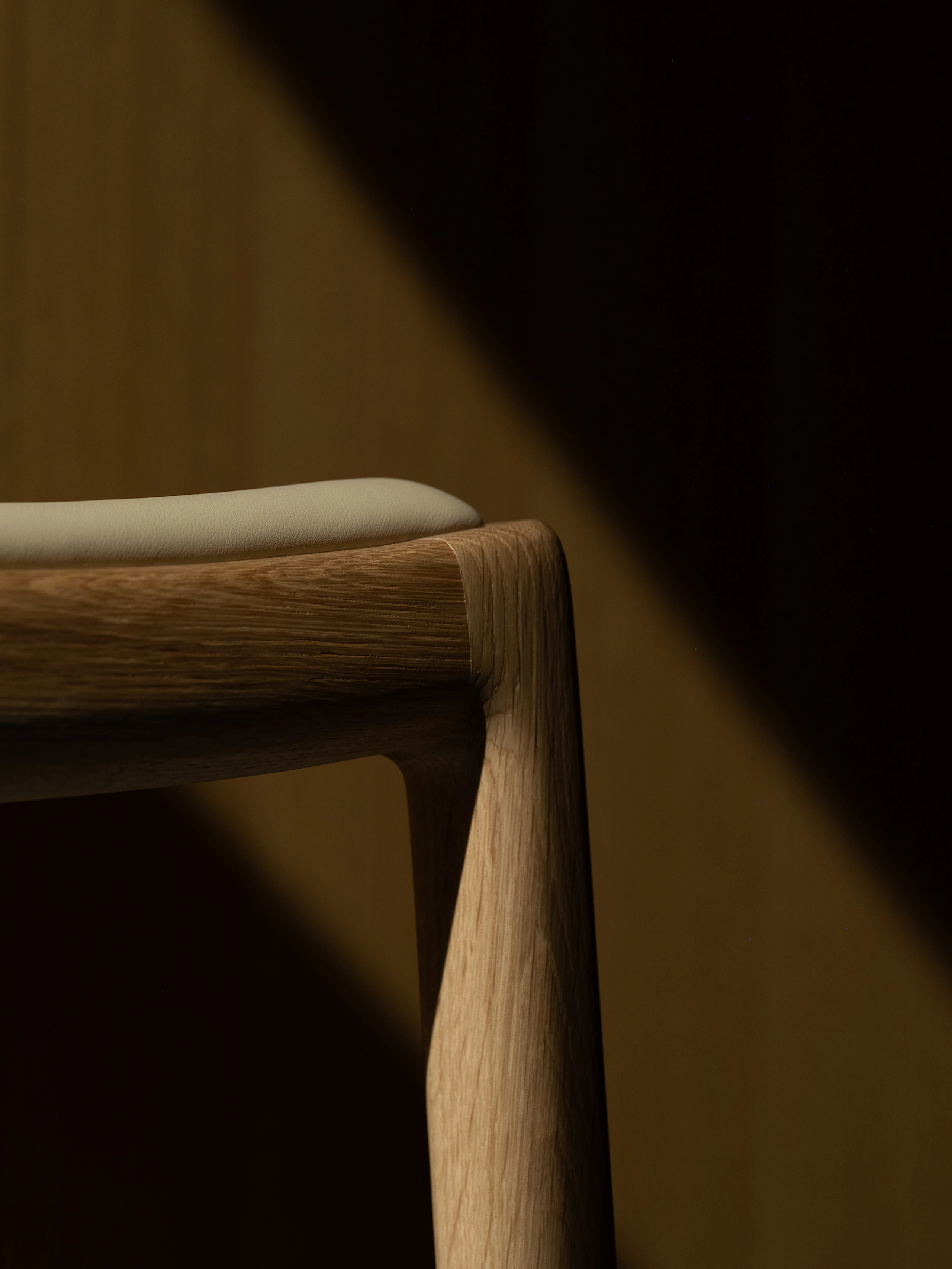 Detail view of a Lijn Stool frame and seat in Natural Oak fully upholstered with Bristol leather in Champagne, viewed from below at an angle.
