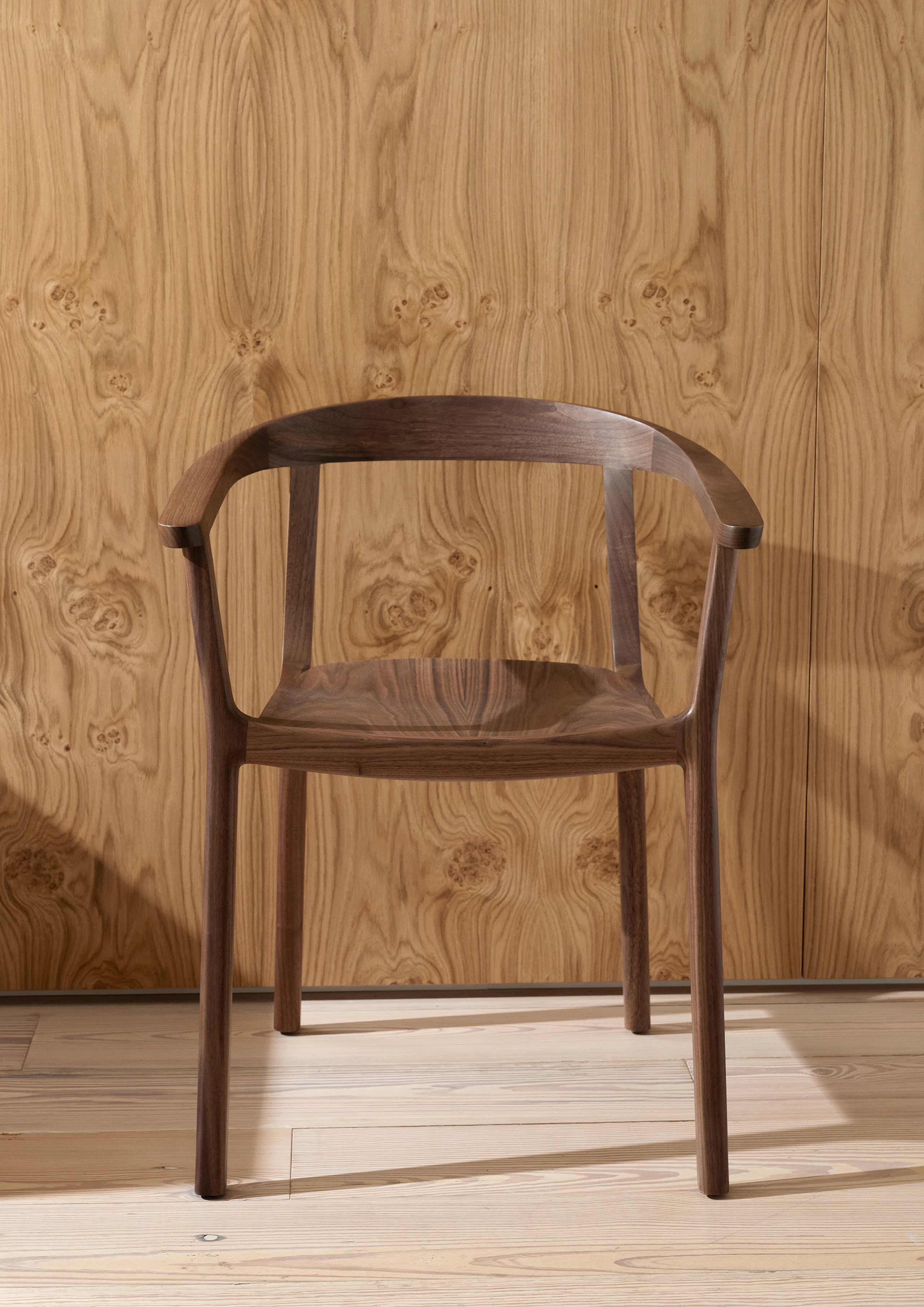 Lijn Armchair designed by Carole Baijings in Natural Walnut, viewed from the front against a veneer wall.