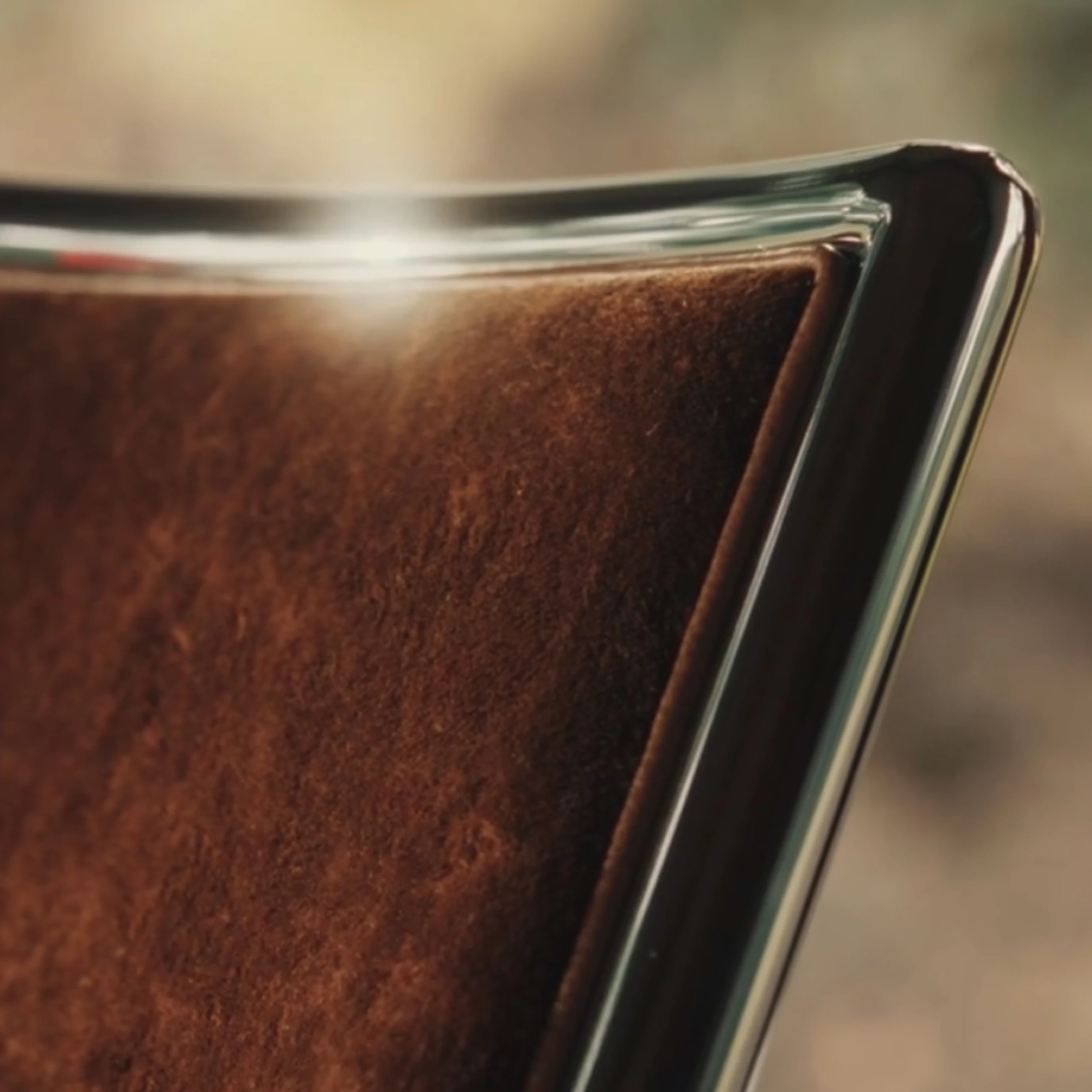 Detail view of a Scissor Chairs designed by Ward Bennett, upholstered in Linen Velvet in Curcuma with a chrome frame, viewed at an angle.