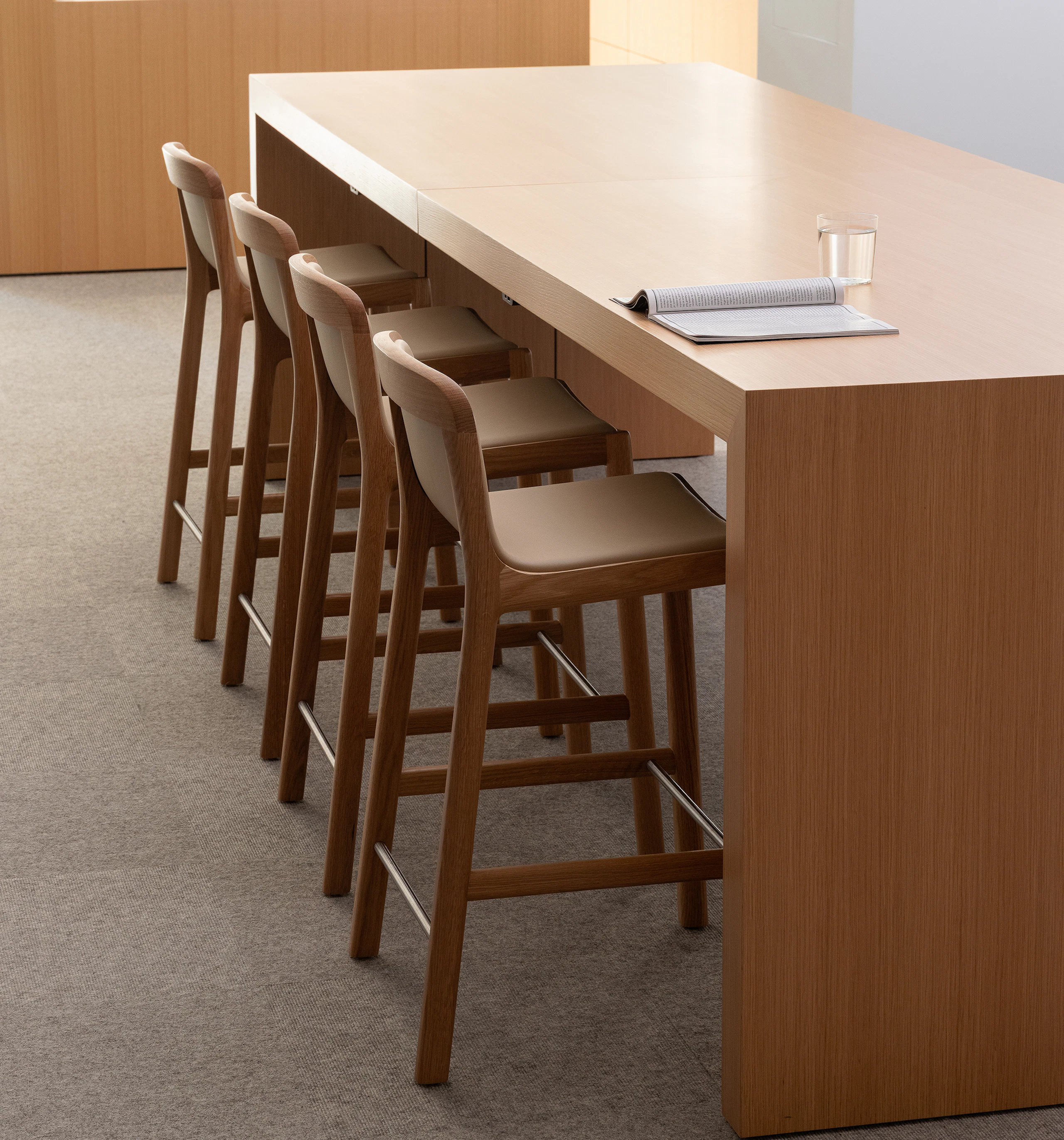 Four counter height Lijn Stools in Natural Oak fully upholstered with Bristol leather in Champagne with a JD Waterfall Table in Natural Rift Cut Oak, viewed at an angle.