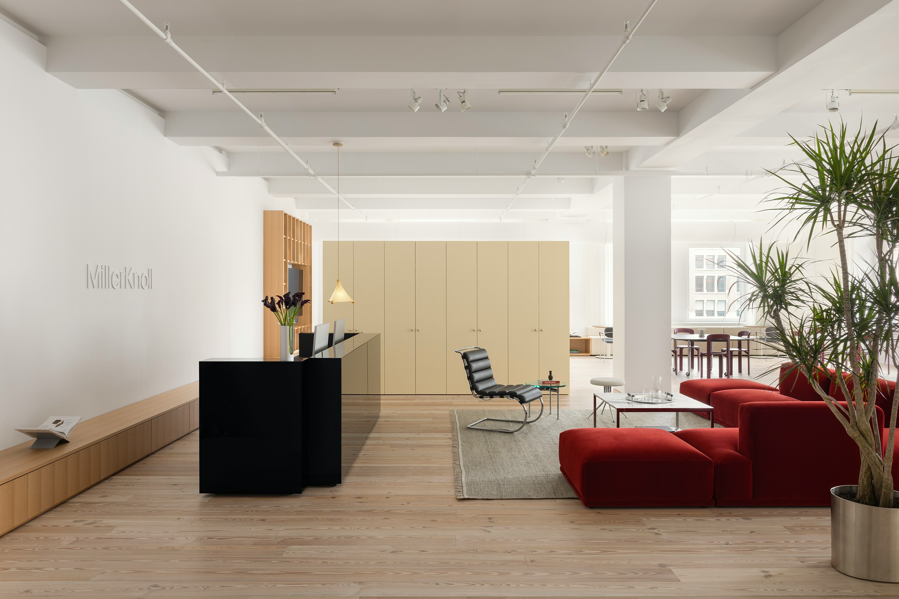 A reception area furnished with a large red sofa, a coffee table, and side chair at the MillerKnoll New York City showroom.