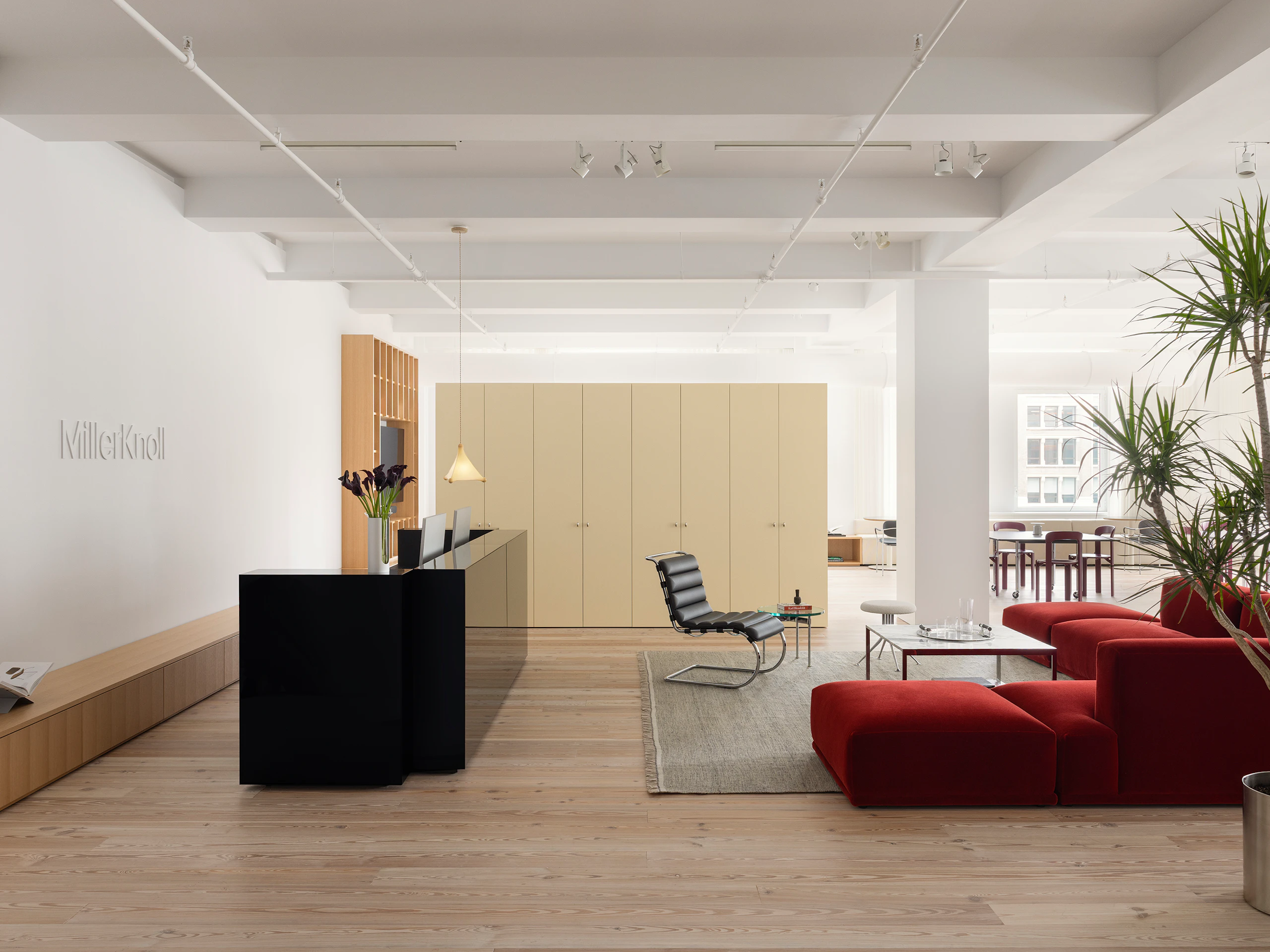 A reception area furnished with a large red sofa, a coffee table, and side chair at the MillerKnoll New York City showroom.