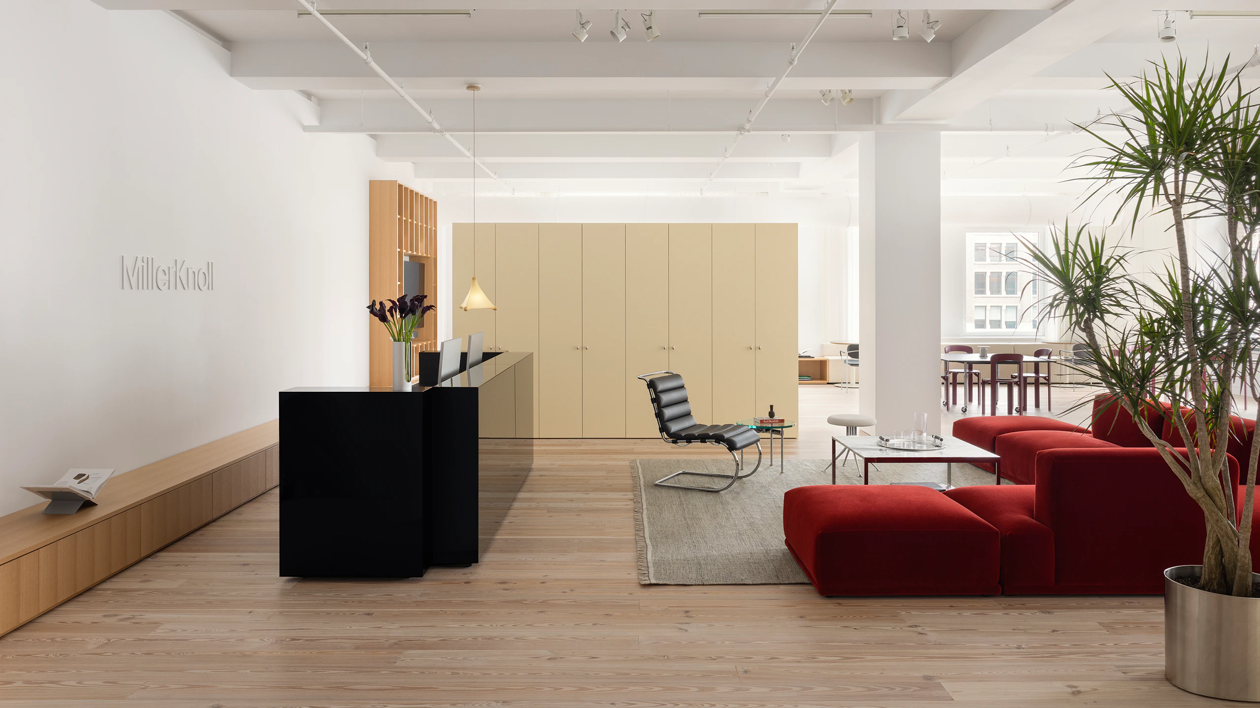 A reception area furnished with a large red sofa, a coffee table, and side chair at the MillerKnoll New York City showroom.