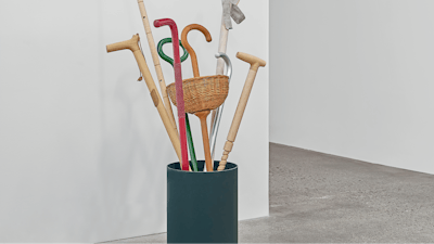 A green basket of assorted walking sticks and canes in red, green, wood, and other miscellaneous materials.
