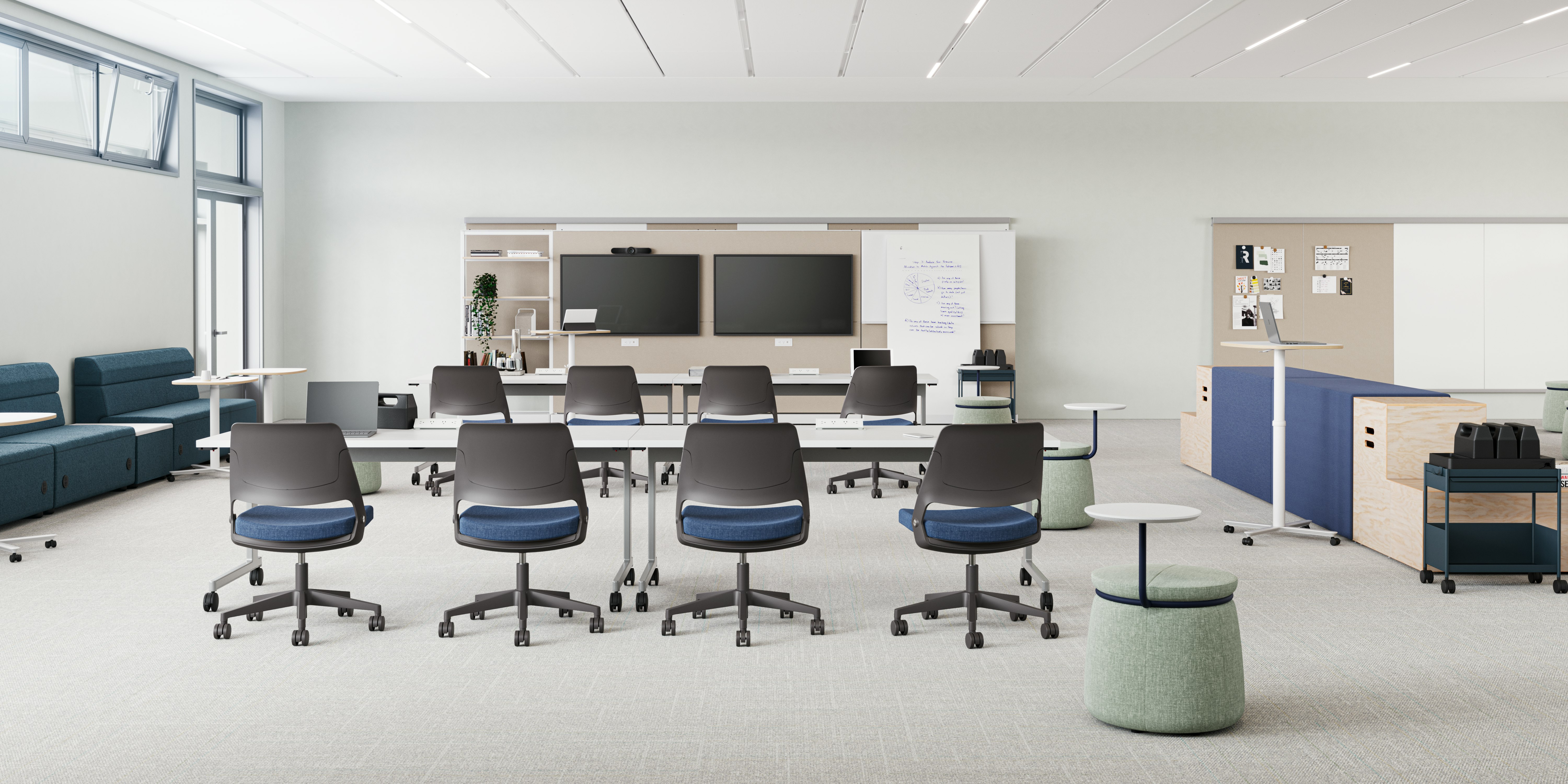  Modern classroom with blue modular seating units, small round tables, and a long white table with a laptop and teal chairs. Focus on collaborative and flexible workspaces.
