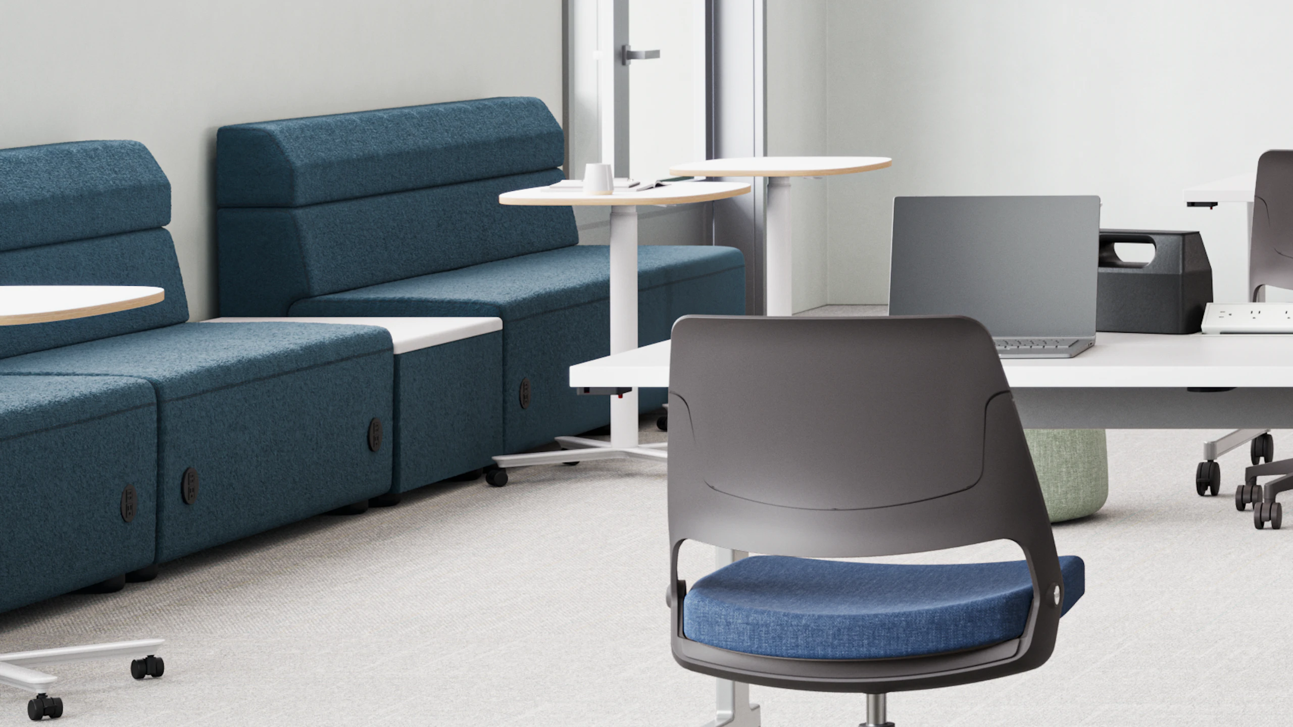 Modern classroom with blue modular seating units, small round tables, and a long white table with a laptop and teal chairs. Focus on collaborative and flexible workspaces.