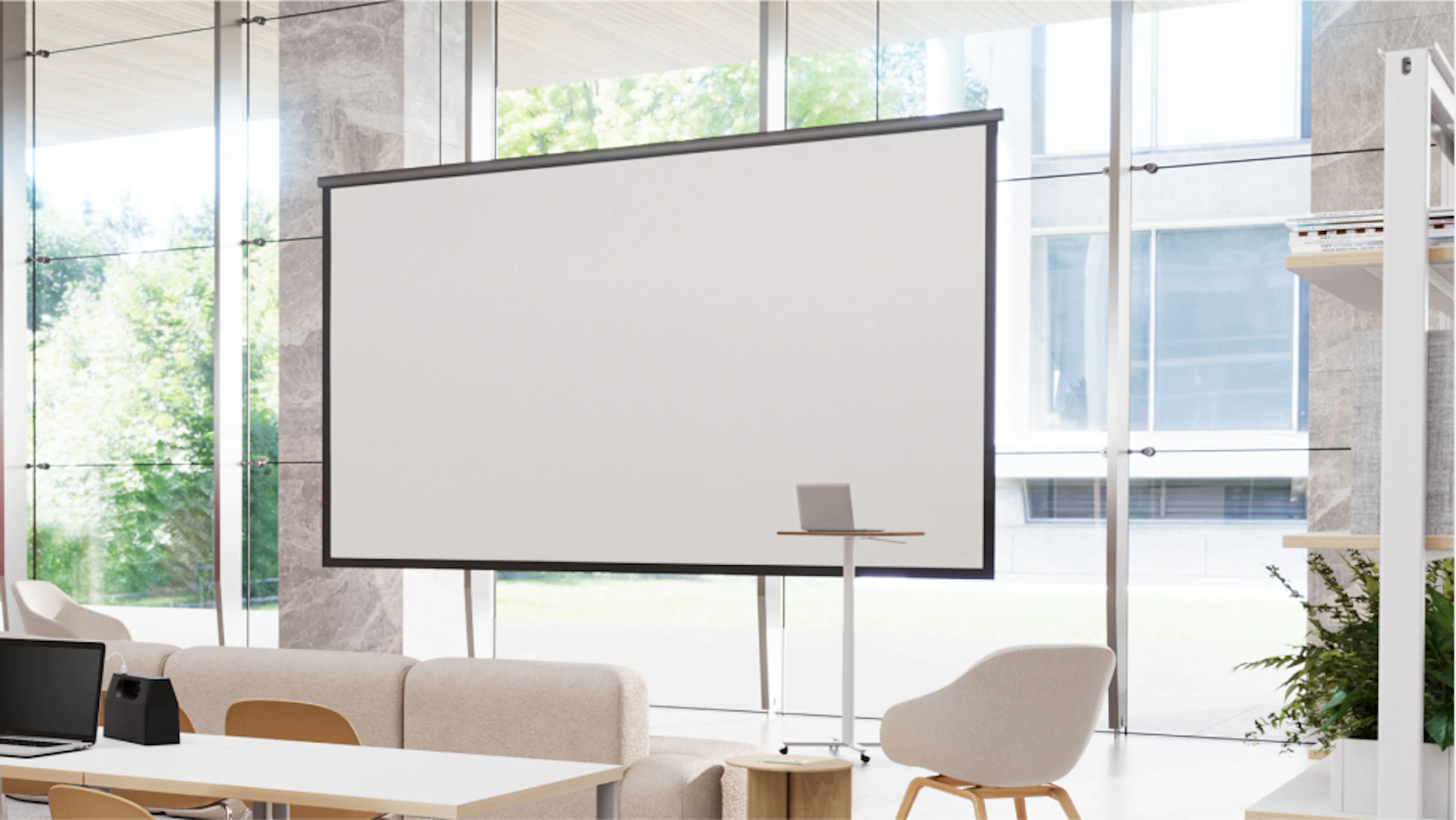 Modern space with large screen, laptop on stand, and comfortable seating. Large windows overlook green outdoor space.