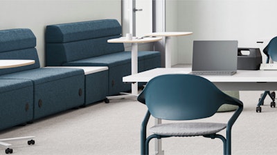 Aula moderna con unidades de asientos modulares azules, pequeñas mesas redondas y una mesa blanca larga con una computadora portátil y sillas color verde azulado. Centrarse en espacios de trabajo colaborativos y flexibles.