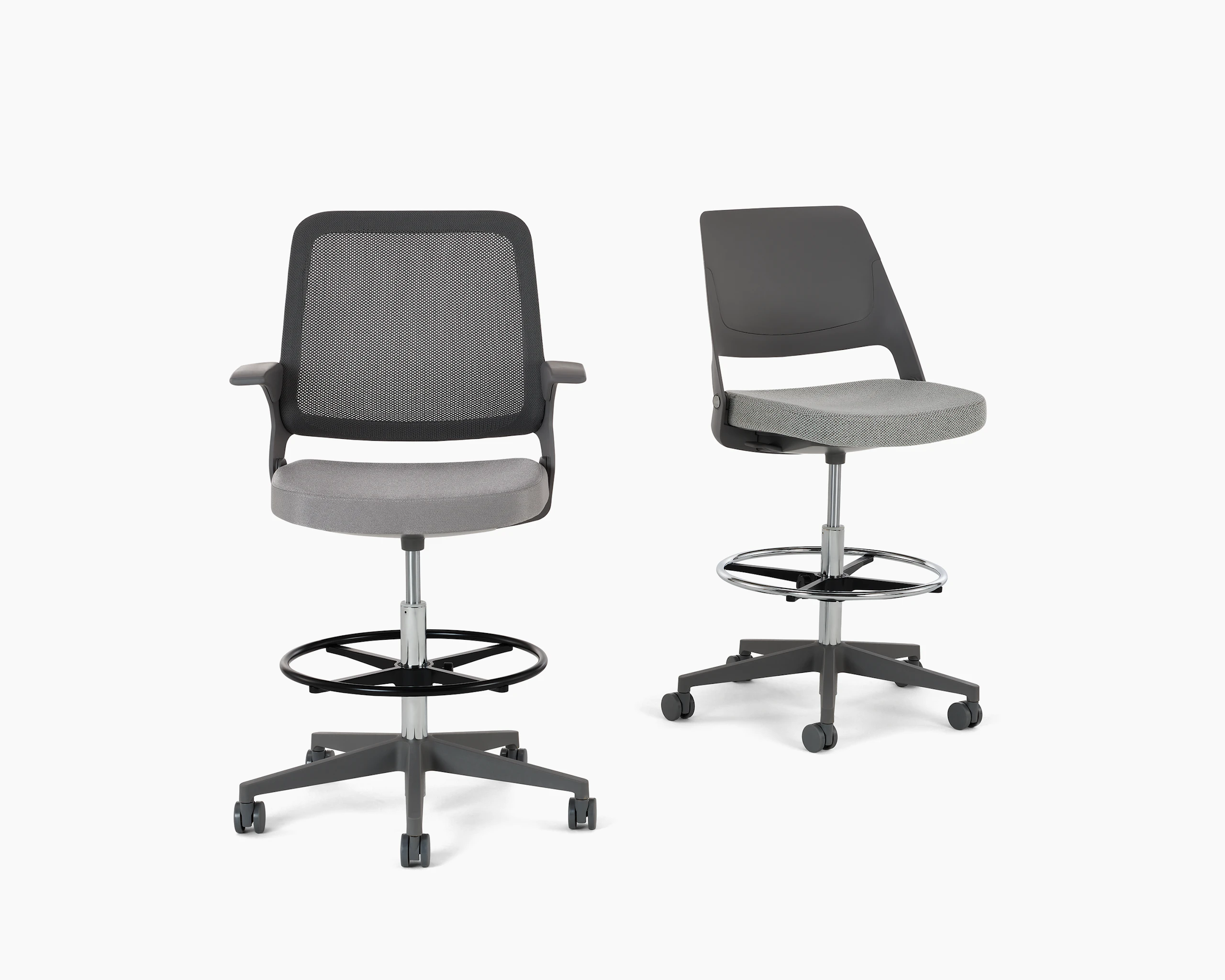 Ollo High Task Chair Stool with a Gunmetal color knit back, medium grey frame and base, fixed arms, a 5-star plastic base, and hard casters, with a silver cylinder and a silver foot ring. The cushioned seat is upholstered in Reflect textile in the color 4 Steel (grey). Next to an Ollo High Task Chair Stool with a medium grey shell back and base, no arms, a 5-star plastic base, and hard casters, with a silver cylinder and a silver foot ring. The cushioned seat is upholstered in Facet textile in the color 2 Mica (light grey). White background. White baground