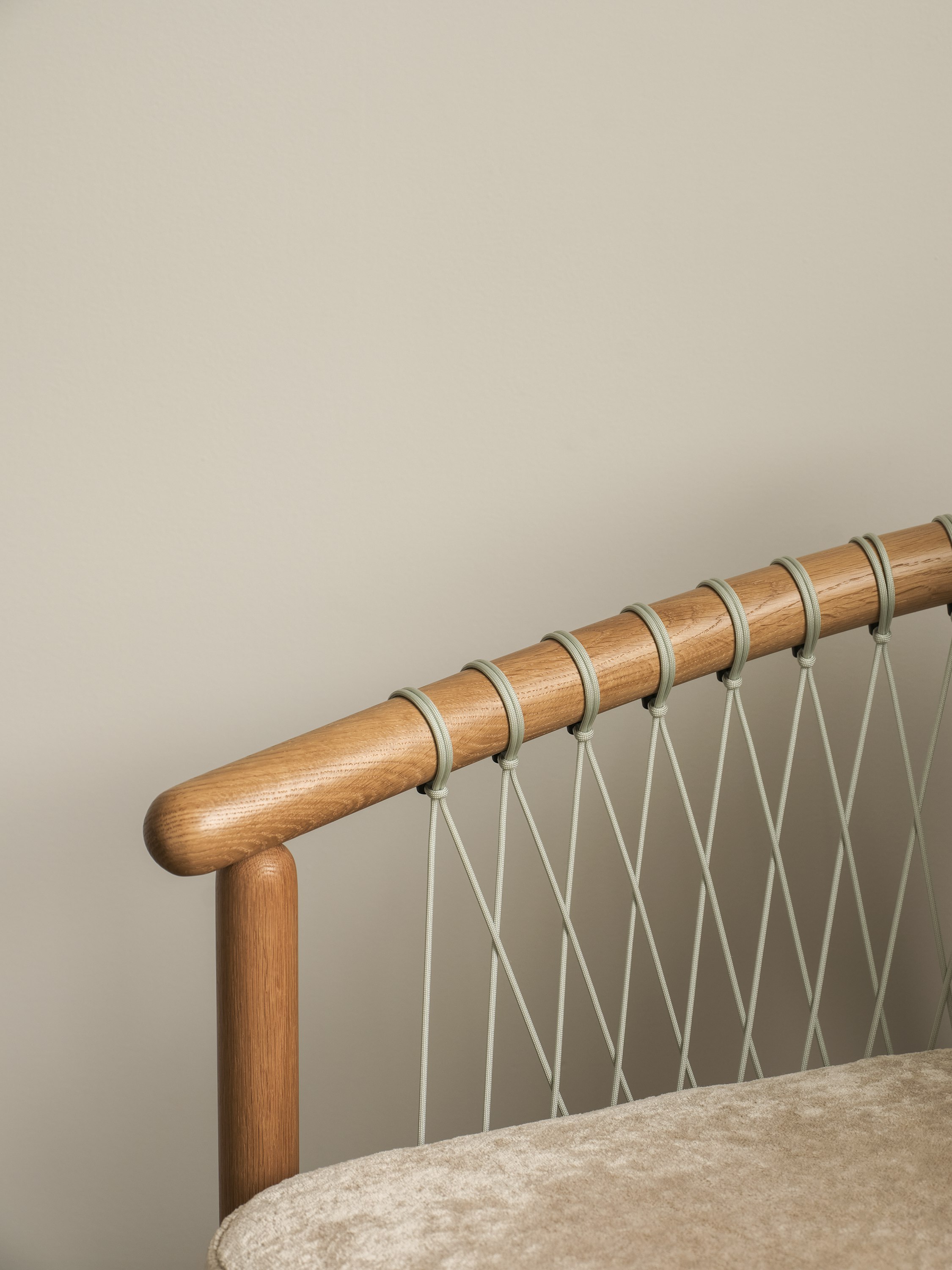 Detail view of a Crosshatch Chair arm and seat with a Natural Oak frame and grey parachute cords, upholstered with Linen Velvet in Obelisk, viewed at an angle.