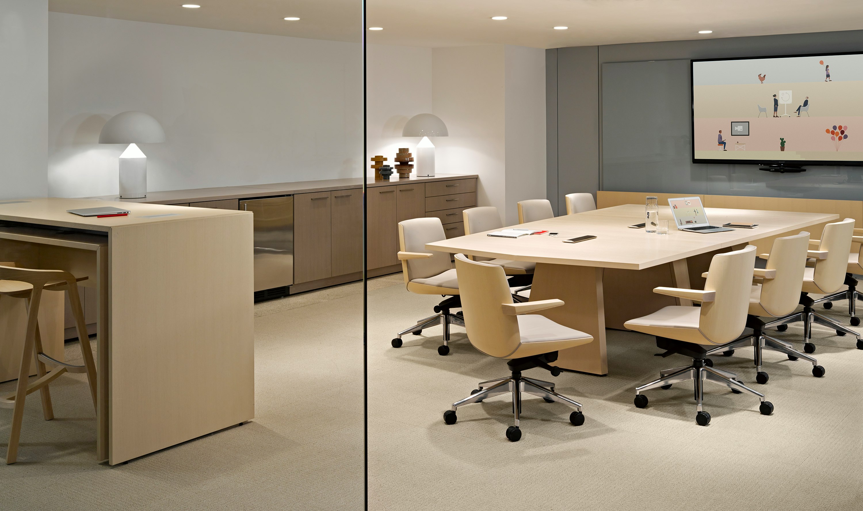 A large wall-hung monitor overlooks a Geiger Elsi video conference table surrounded by several ivory-colored Clamshell office chairs.