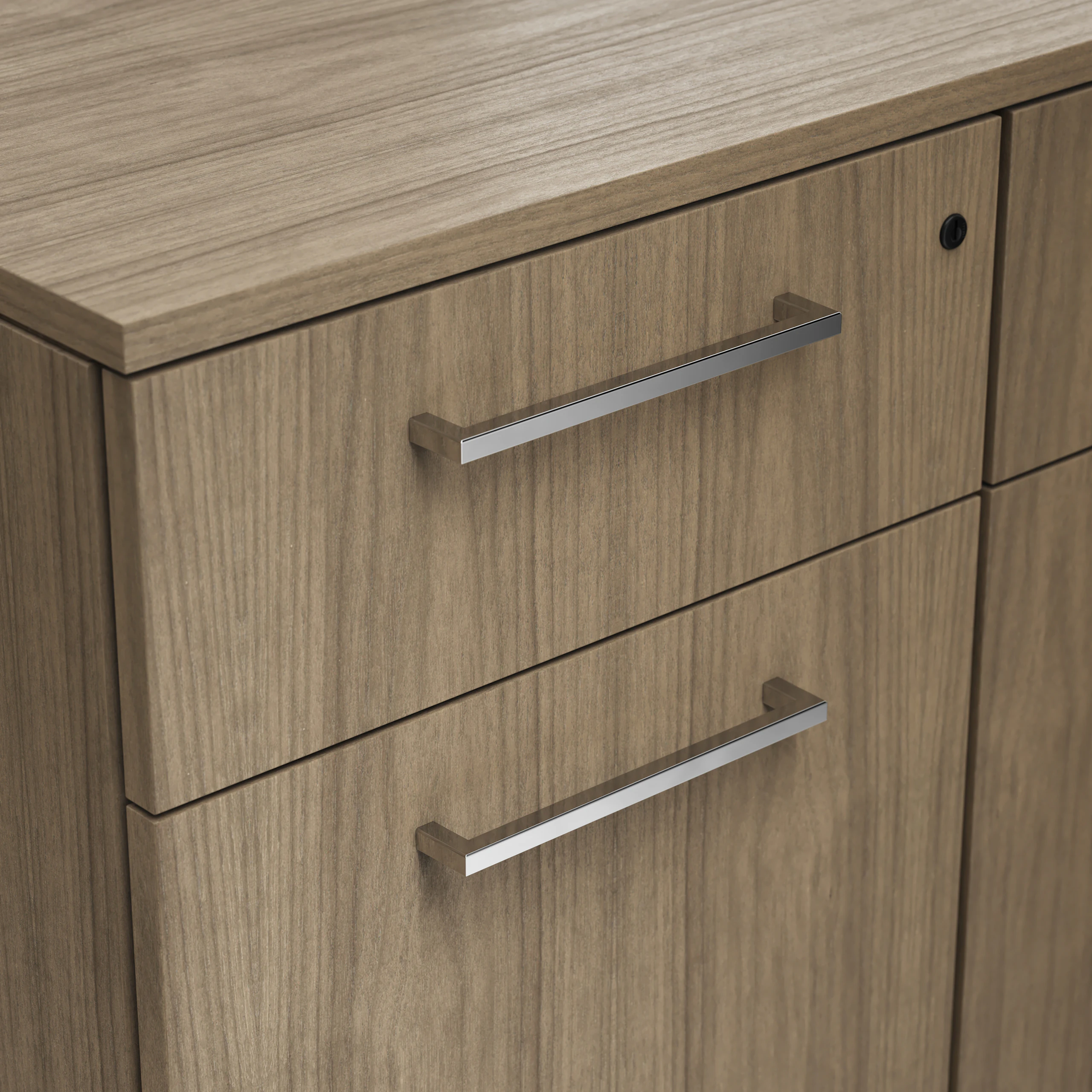 Detail shot of the Geiger One Casegoods rectangular pull option in Chrome on a Natural Flat Cut Walnut drawer front viewed from an angle.