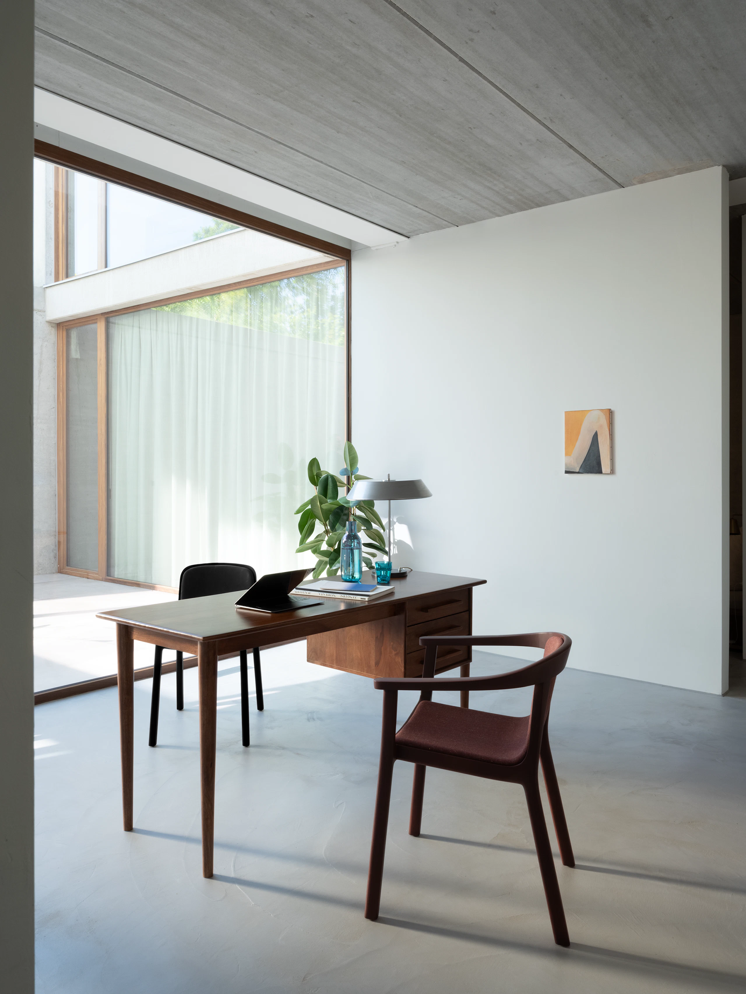 Lijn Armchair in Red Clay with an upholstered seat beside a desk with a Lijn Side Chair in Ebonized oak in a residential office setting, viewed at an angle.