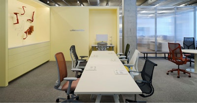 A variety of Herman Miller office chairs, including Cosm chairs, Mirra 2 chairs, and Sayl chairs, arranged around a white conference table at the Herman Miller seating lab at MillerKnoll Design Days