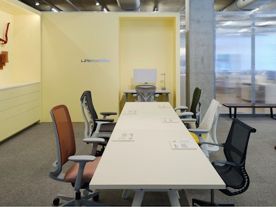 A variety of Herman Miller office chairs, including Cosm chairs, Mirra 2 chairs, and Sayl chairs, arranged around a white conference table at the Herman Miller seating lab at MillerKnoll Design Days