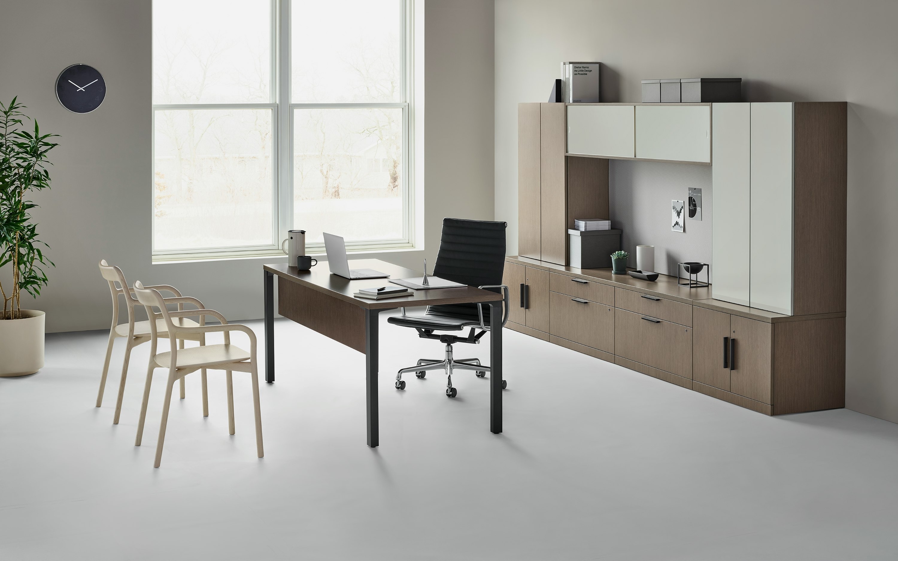 A traditional Canvas Private Office with dark wood and glass storage, with a black Eames Aluminum Group chair, and two light wood Branca side chairs.