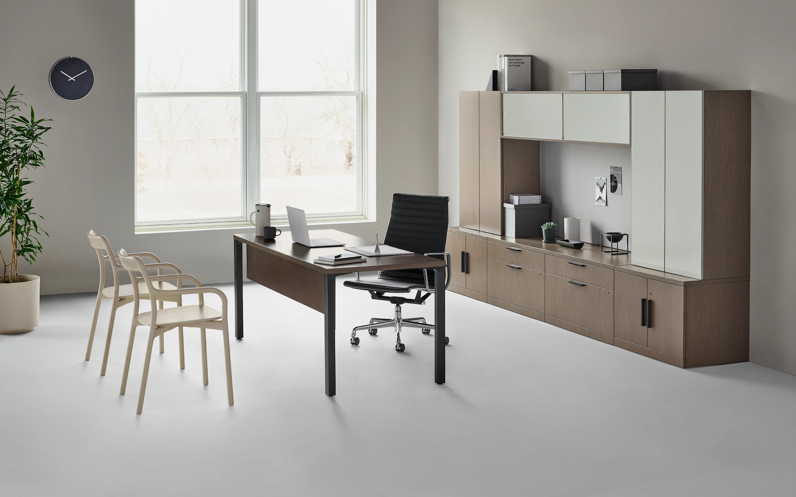 A traditional Canvas Private Office with dark wood and glass storage, with a black Eames Aluminum Group chair, and two light wood Branca side chairs.