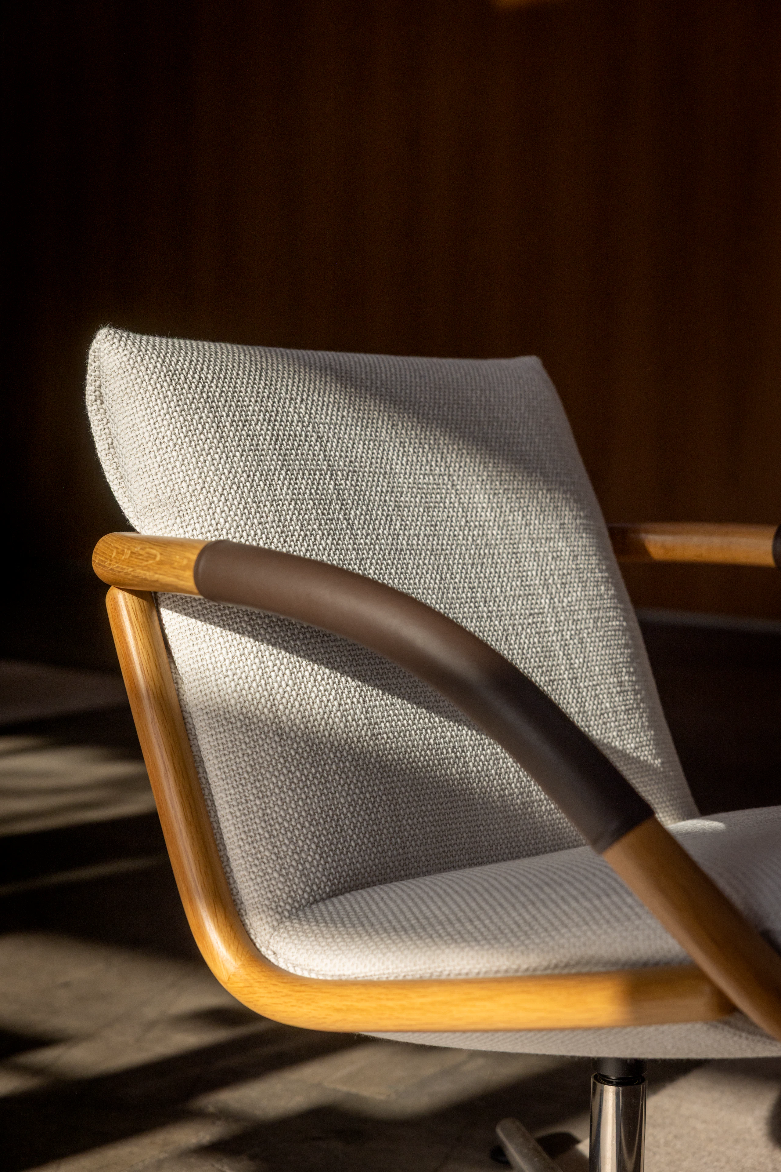 Detail view of a Full Loop Lounge Chair upholstered with Capri in Snow with an Oak frame and leather-wrapped arms, viewed at an angle in a showroom setting.