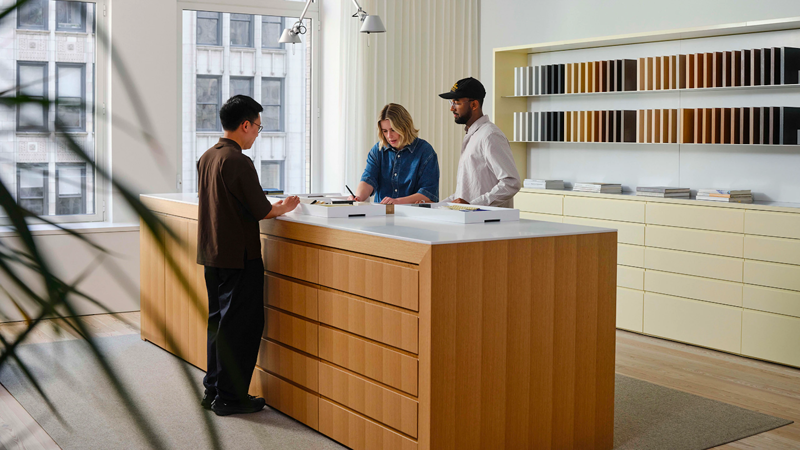 Three people working at a large island in a MillerKnoll showroom. Rows of different colored materials can be seen along the back wall.