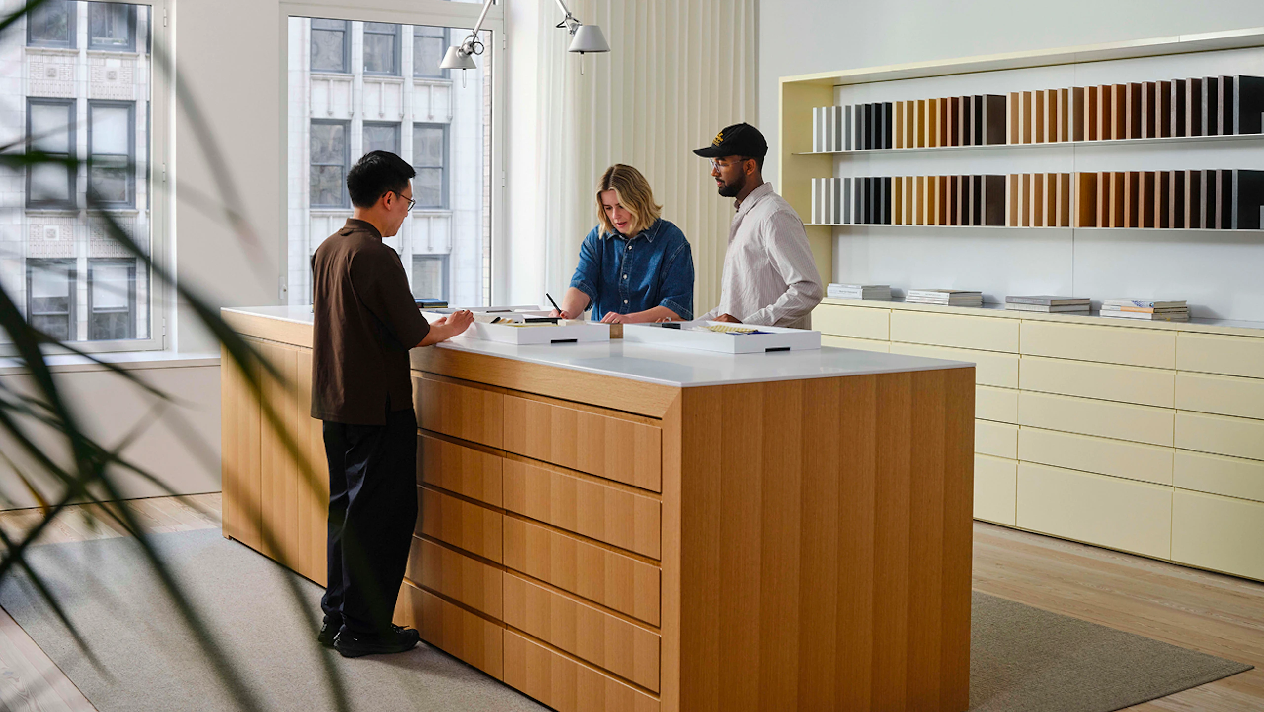 Three people working at a large island in a MillerKnoll showroom. Rows of different colored materials can be seen along the back wall.