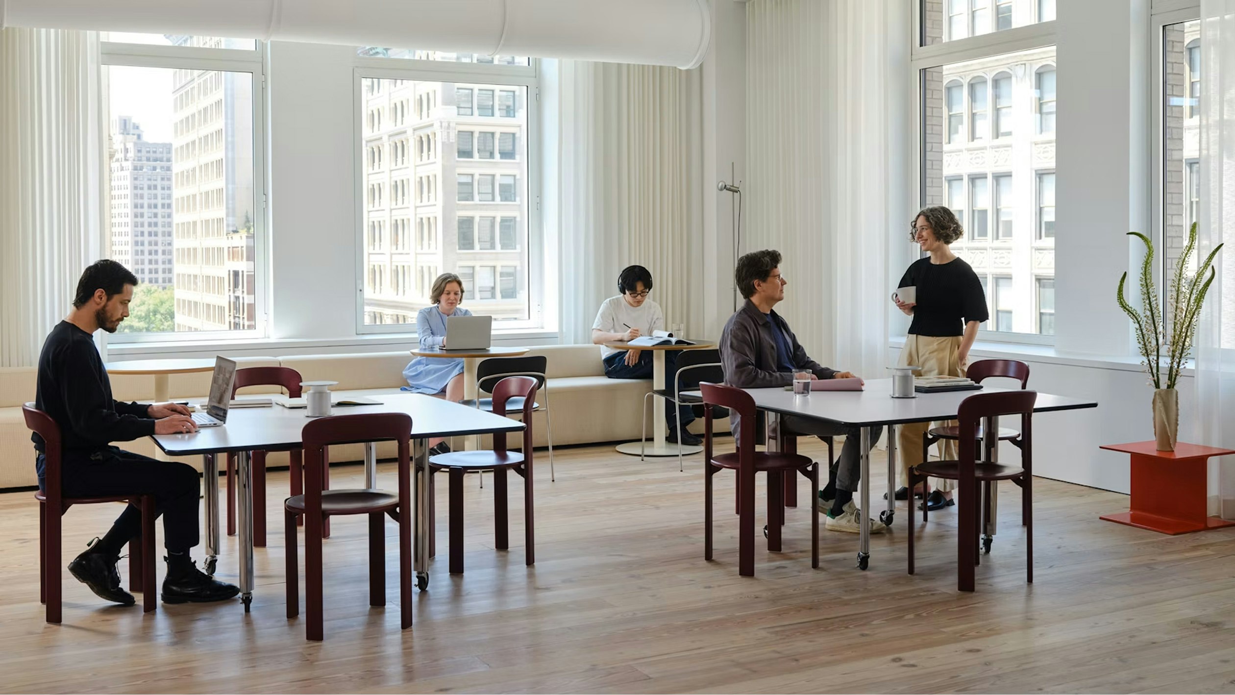 Several people working at the MillerKnoll New York Showroom in a communal space furnished with Rey Chairs from HAY and other furniture from the MillerKnoll portfolio.