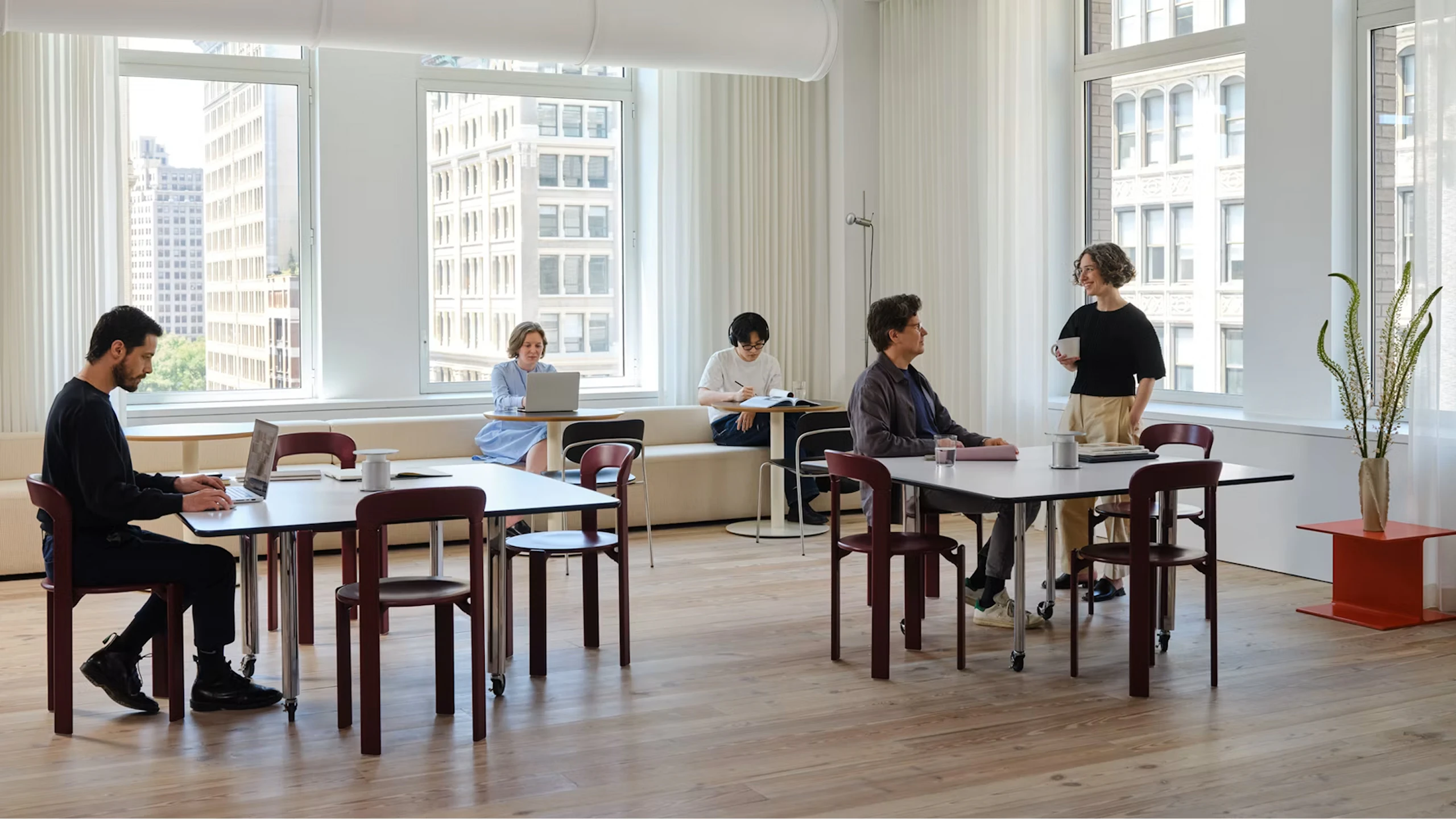 Several people working at the MillerKnoll New York Showroom in a communal space furnished with Rey Chairs from HAY and other furniture from the MillerKnoll portfolio.
