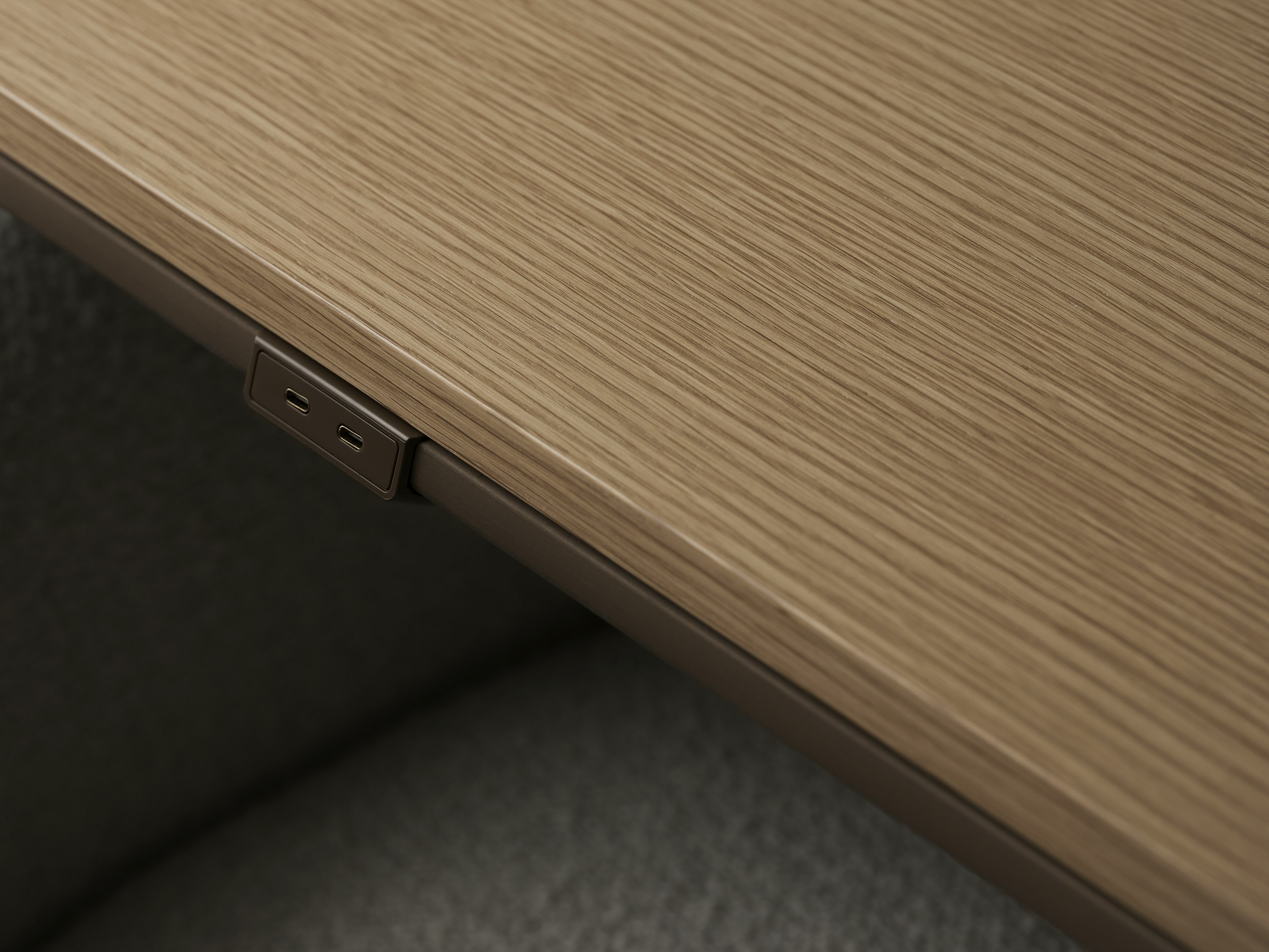 Detail view of the Ascent Conference Table perimeter power in luxe medium bronze with a Natural Rift Cut Oak tabletop, viewed from above at an angle.