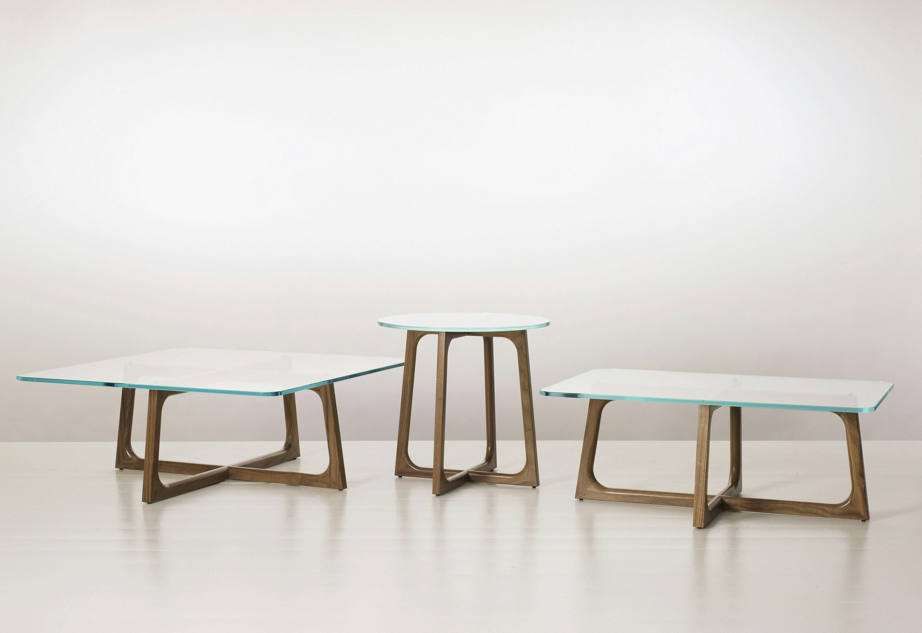 Three Loophole occasional tables of different sizes and shapes, each with a glass top and walnut base.