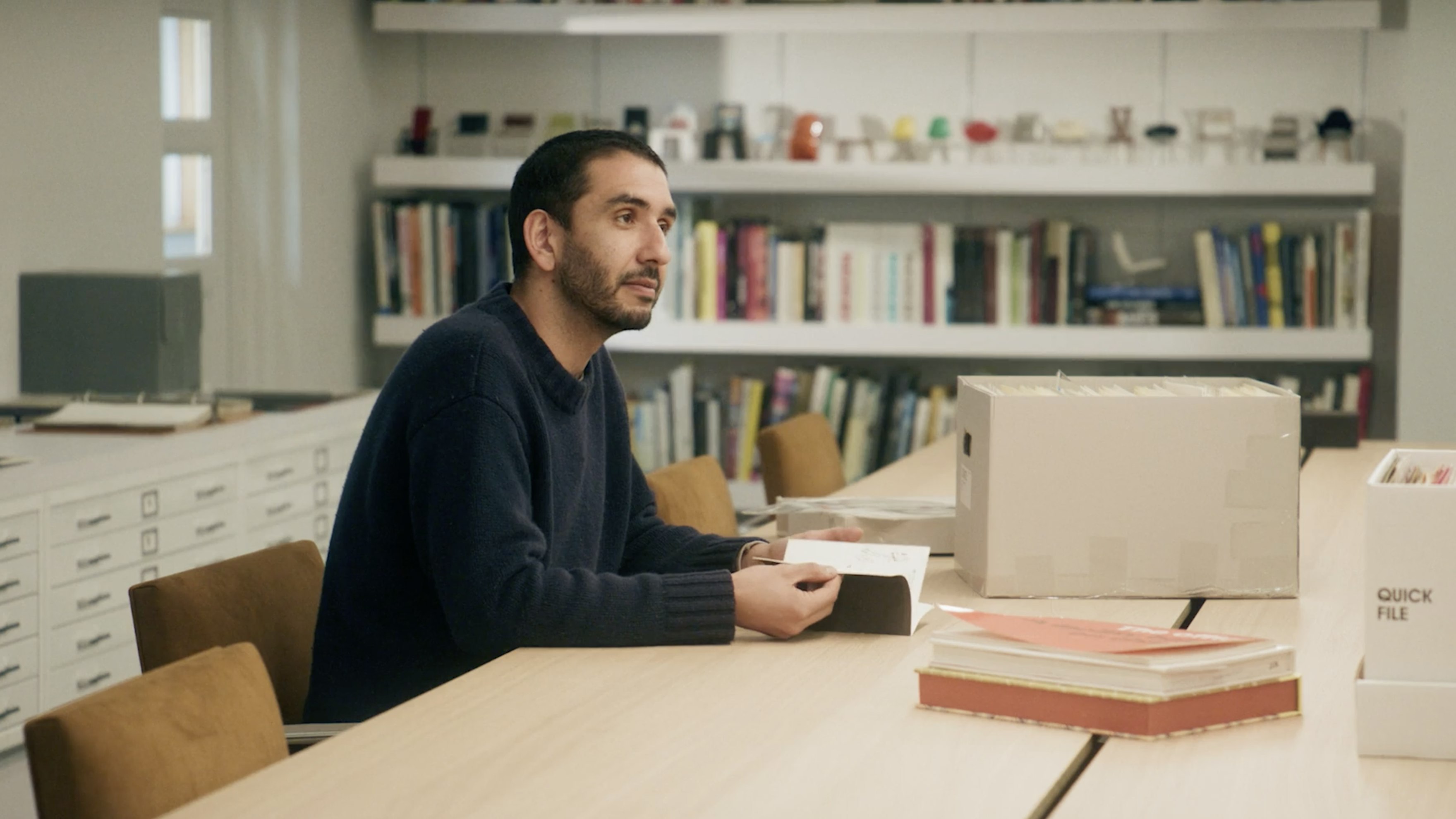 Sina Sohrab seated at a table and turning pages in a small book at the MillerKnoll Archives.