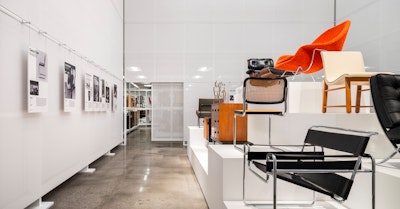 Classic pieces of furniture from the MillerKnoll collective, such as an orange Knoll Womb Chair and black Knoll Barcelona Chair, arranged on white pedestals at the MillerKnoll Archives
