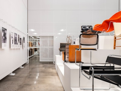 Classic pieces of furniture from the MillerKnoll collective, such as an orange Knoll Womb Chair and black Knoll Barcelona Chair, arranged on white pedestals at the MillerKnoll Archives