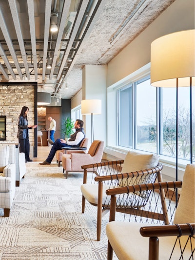 A pair of Geiger Crosshatch Chairs next to windows in a communal seating area in an industrial organization's office. Several people can be seen conversing in the background.