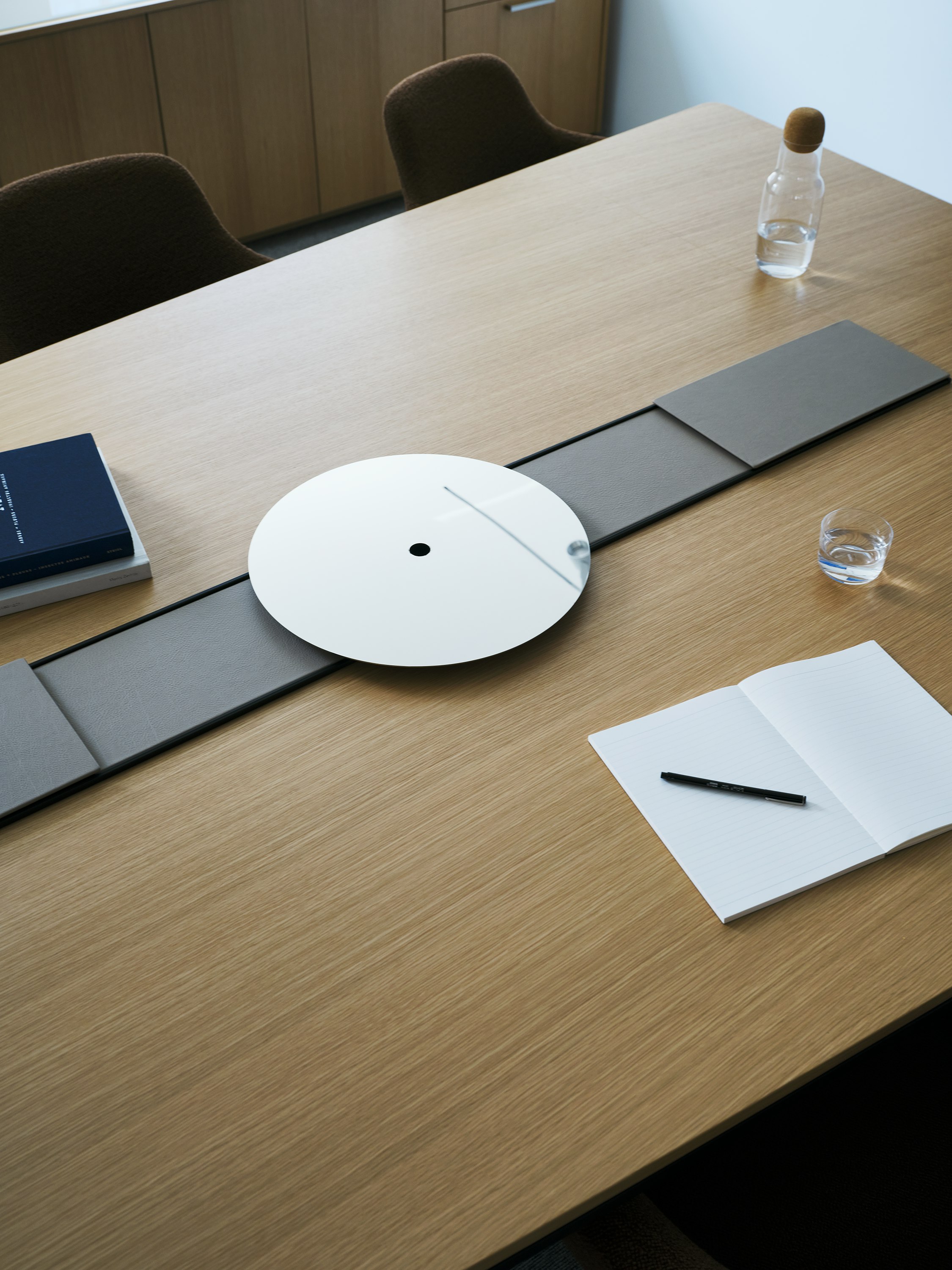 Ascent Conference Table designed by EOOS in Natural Rift Cut Oak with a leather-covered power trough and  chrome accessory tray, viewed from above in a conference room setting.