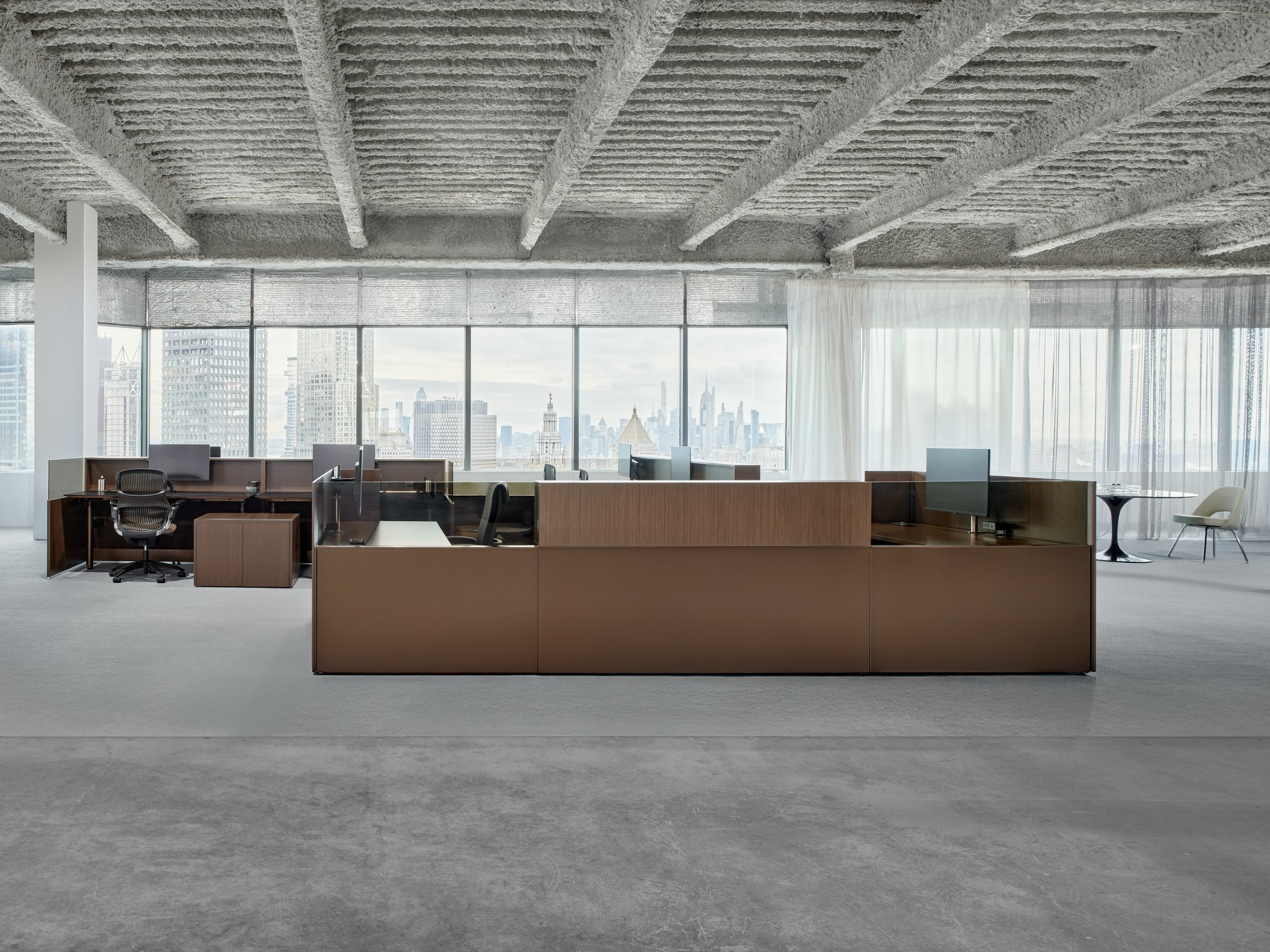 Knoll Skyline workstations with work chairs are grouped together in an open office. The New York city skyline is visible in the windows behind the workstations.