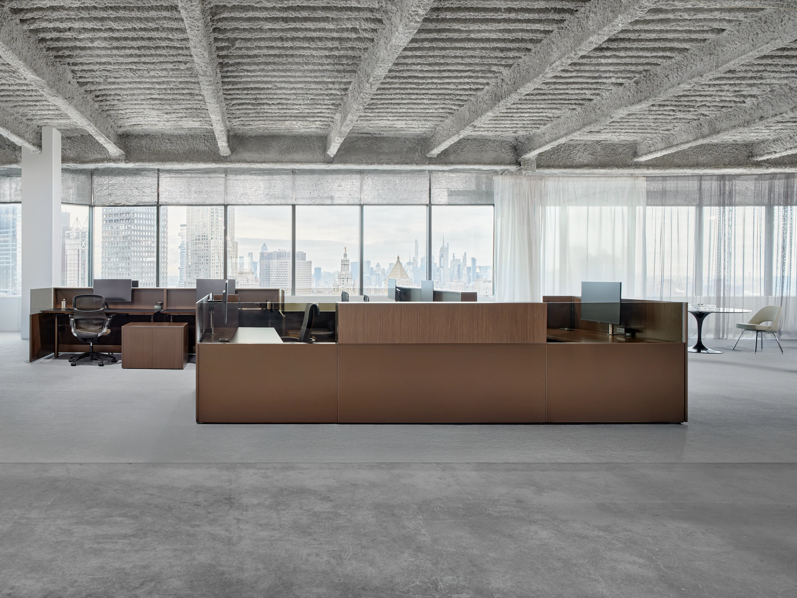 Knoll Skyline workstations with work chairs are grouped together in an open office. The New York city skyline is visible in the windows behind the workstations.