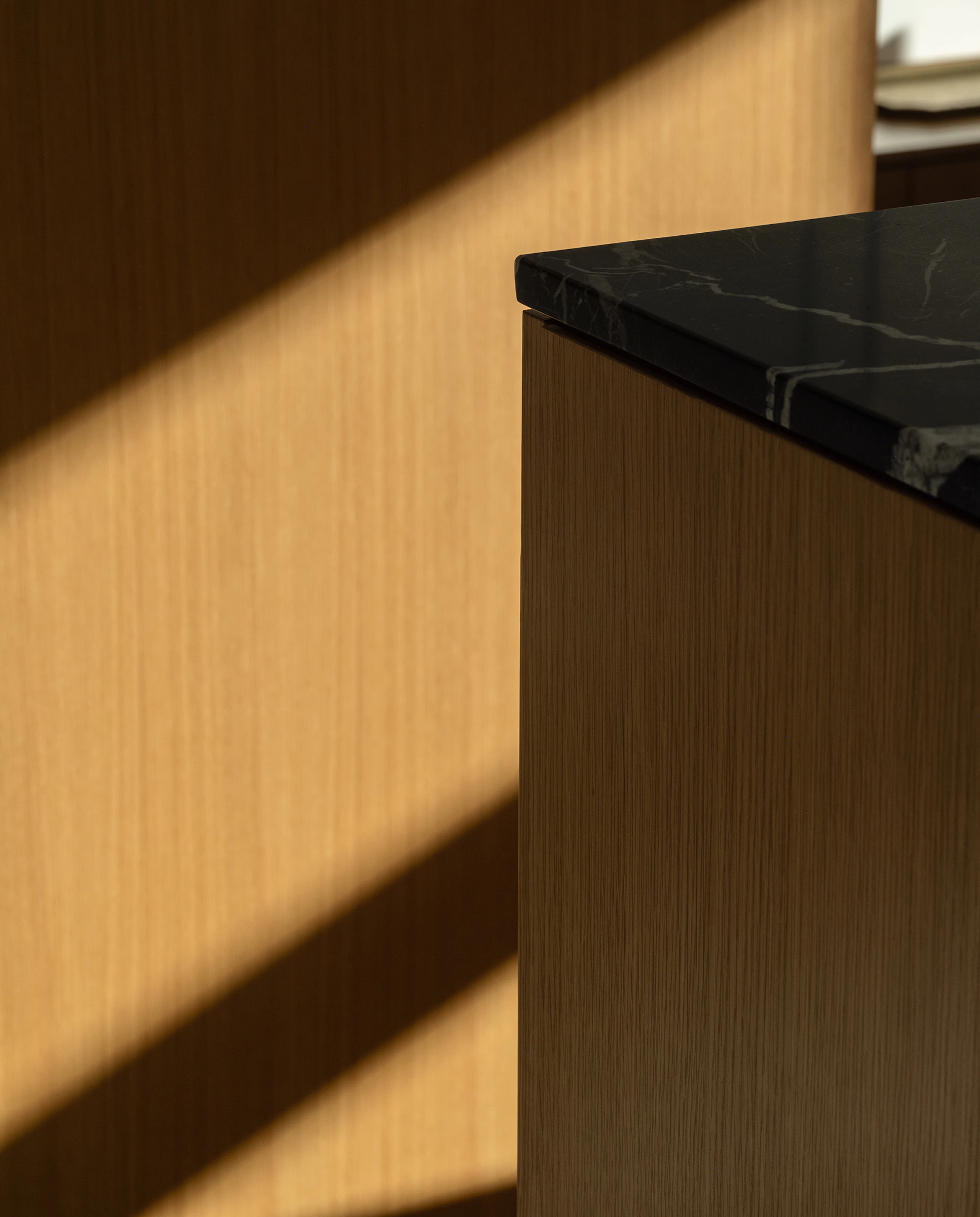 Detail view of a Geiger One Open Plan storage unit in Natural Rift Cut Oak with a Nero Marquina marble top, viewed at an angle.
