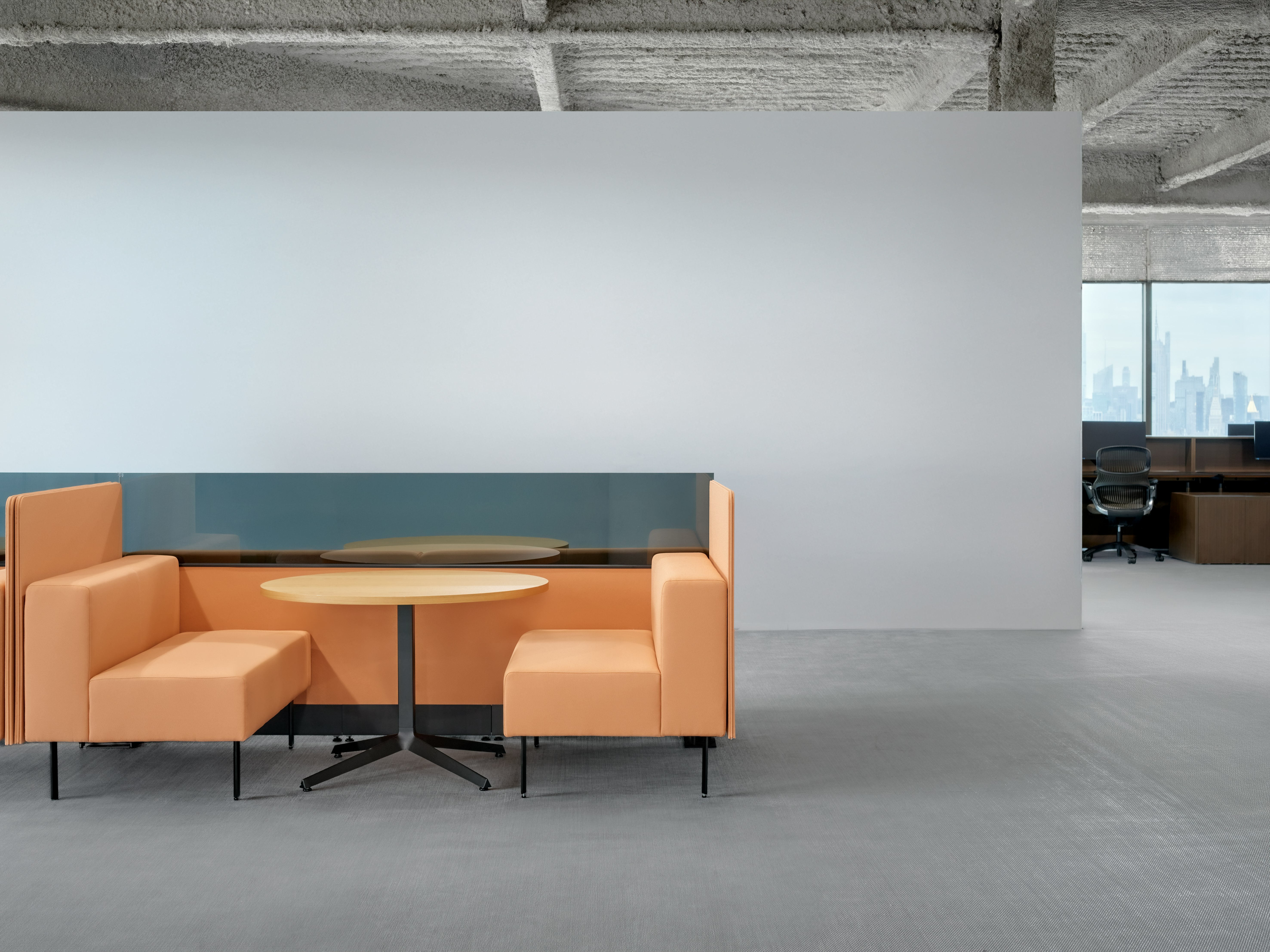 A small meeting table is between two working lounge benches arranged as a small meeting booth. There are privacy screens behind the seats.