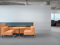 A small meeting table is between two working lounge benches arranged as a small meeting booth. There are privacy screens behind the seats.