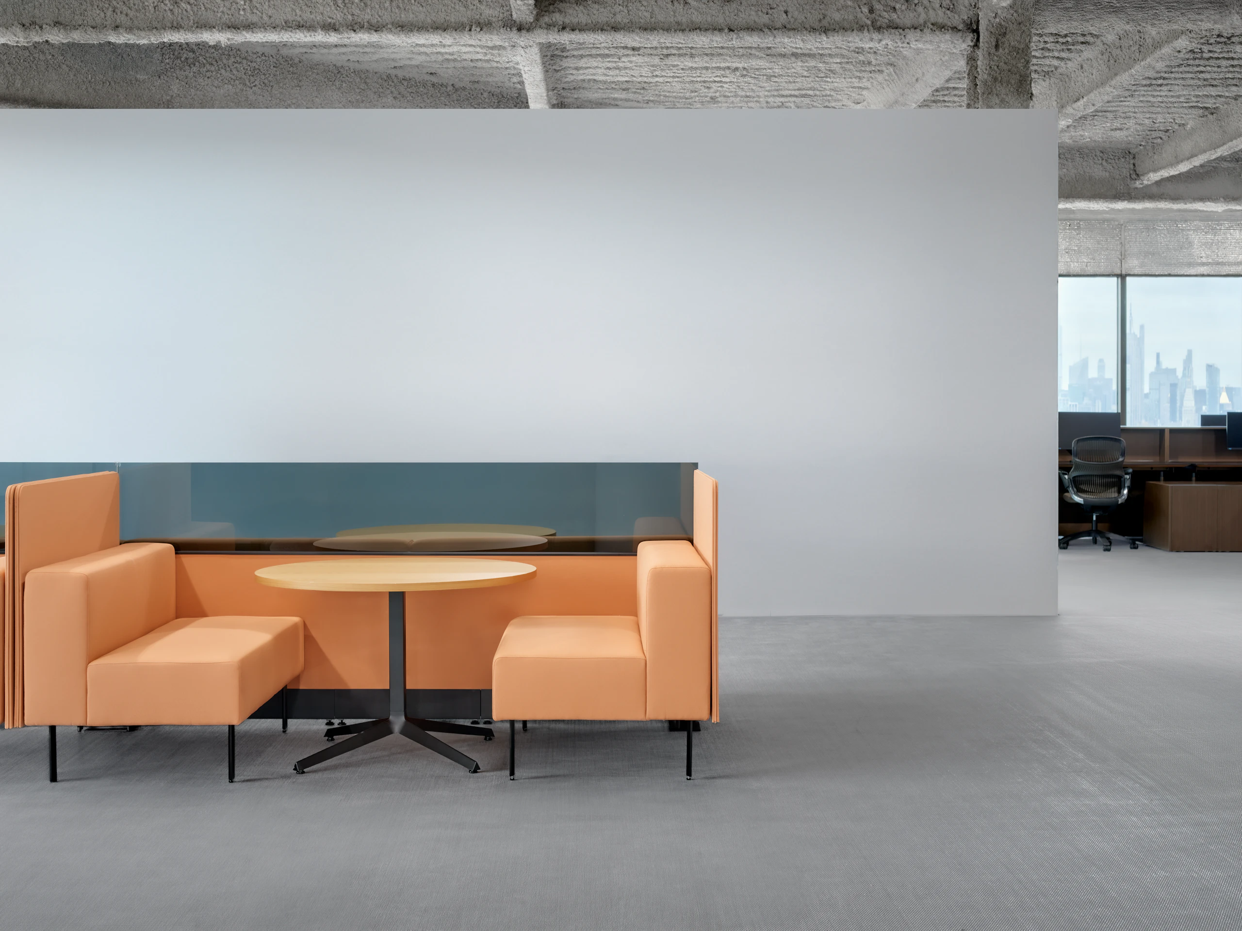 A small meeting table is between two working lounge benches arranged as a small meeting booth. There are privacy screens behind the seats.