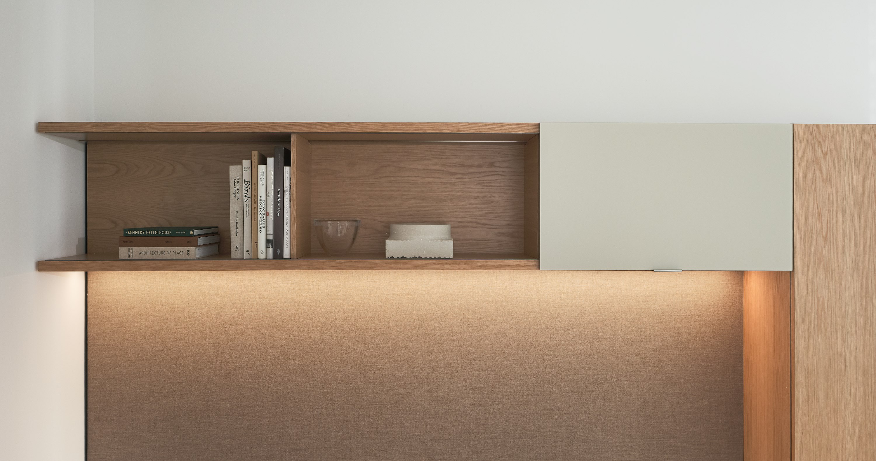 Geiger One Private Office overhead storage featuring an open double shelf in Natural Flat Cut Oak, a Sand back-painted glass sliding door, and integrated lighting, shown from the front.
