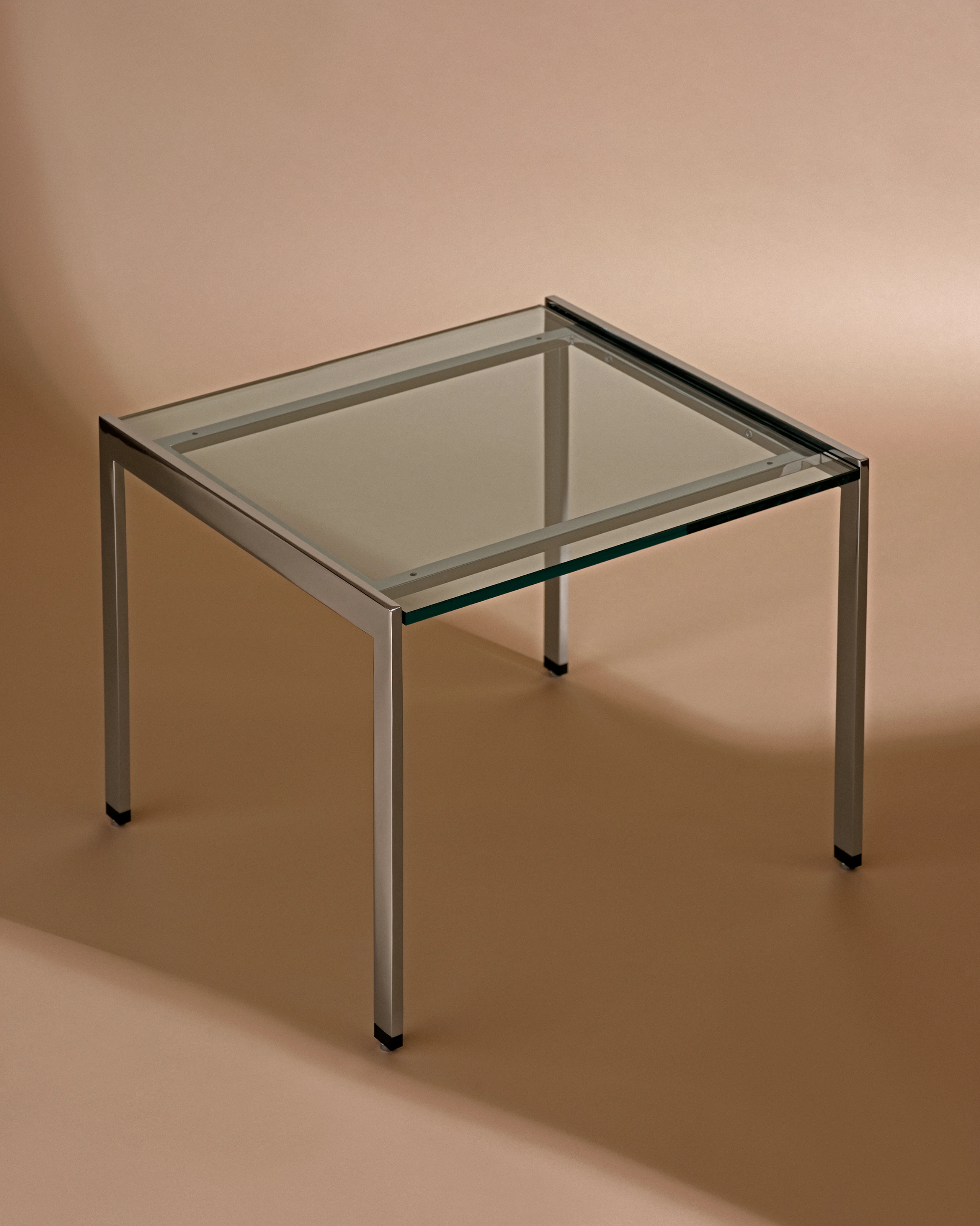 H Frame Side Table designed by Ward Bennett with a clear glass top and chrome frame, shown at an angle against a neutral studio background.