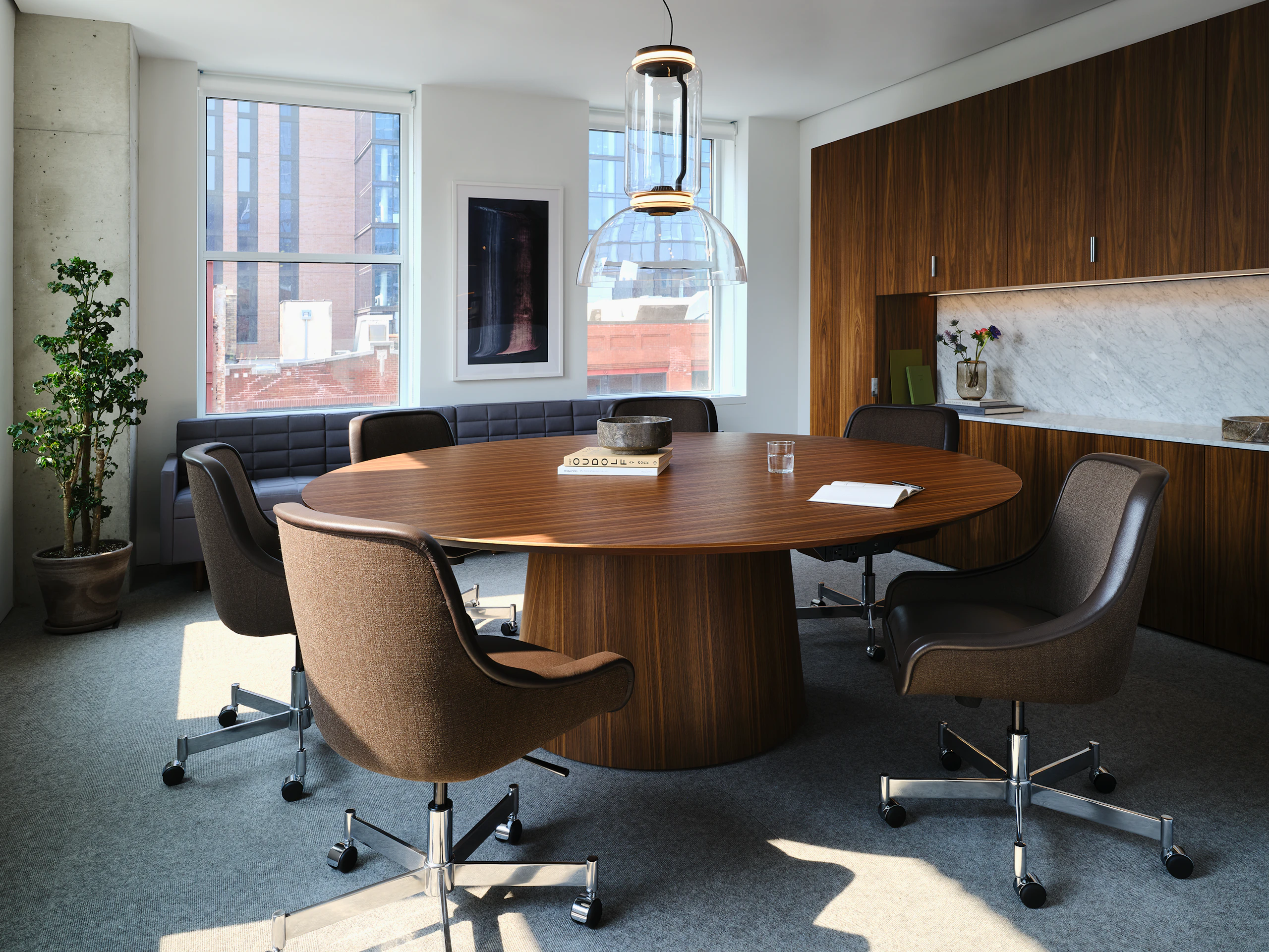 JD Meeting Table in Natural Quarter Cut Walnut with round top and tapered base shown at an angle surrounded by Bumper Chairs in front of a Geiger One workwall.