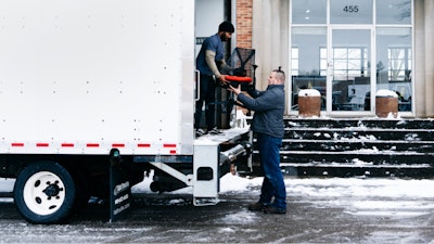 Two people loading a Sayl Chair by Herman Miller into a white delivery truck.