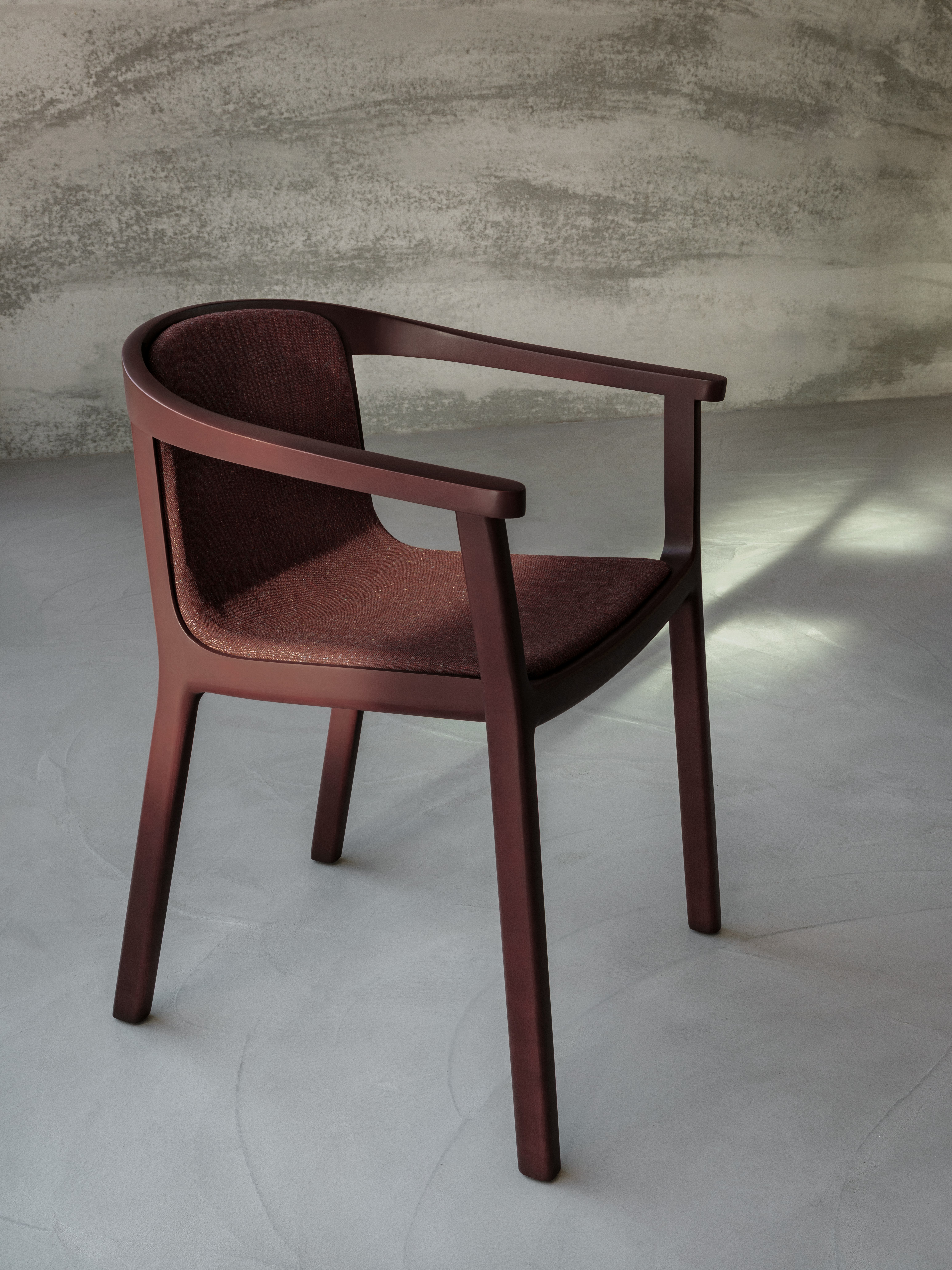 Lijn Chair designed by Carole Baijings for Geiger with upholstered seat and back and tinted wood frame in Red Clay viewed at an angle in a styled environment.