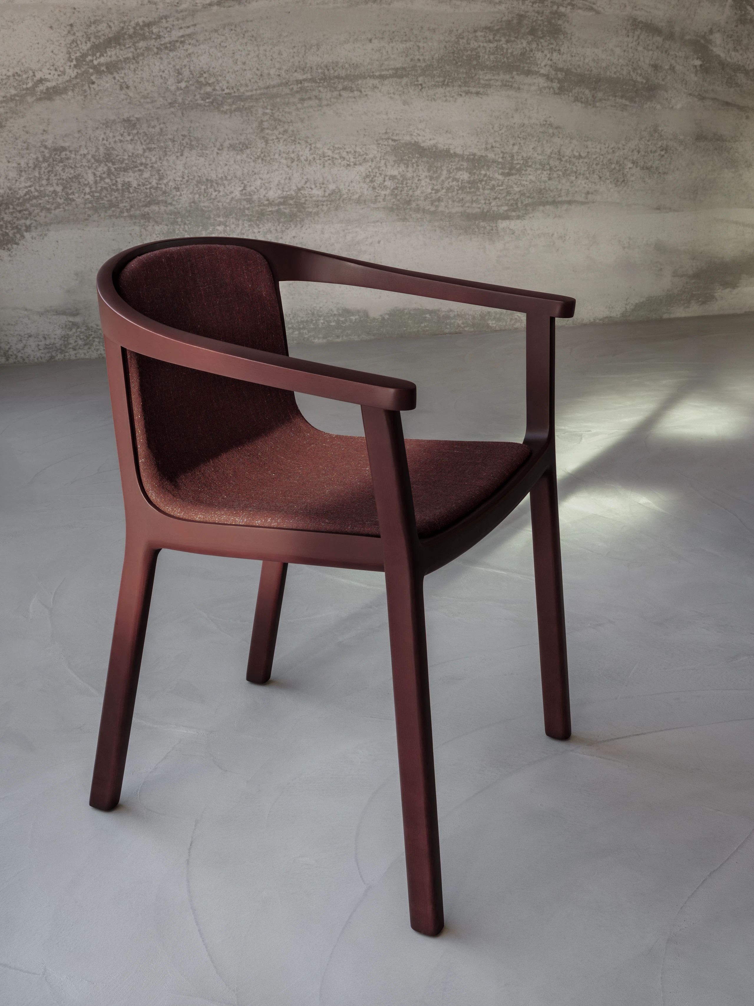 Lijn Chair designed by Carole Baijings for Geiger with upholstered seat and back and tinted wood frame in Red Clay viewed at an angle in a styled environment.