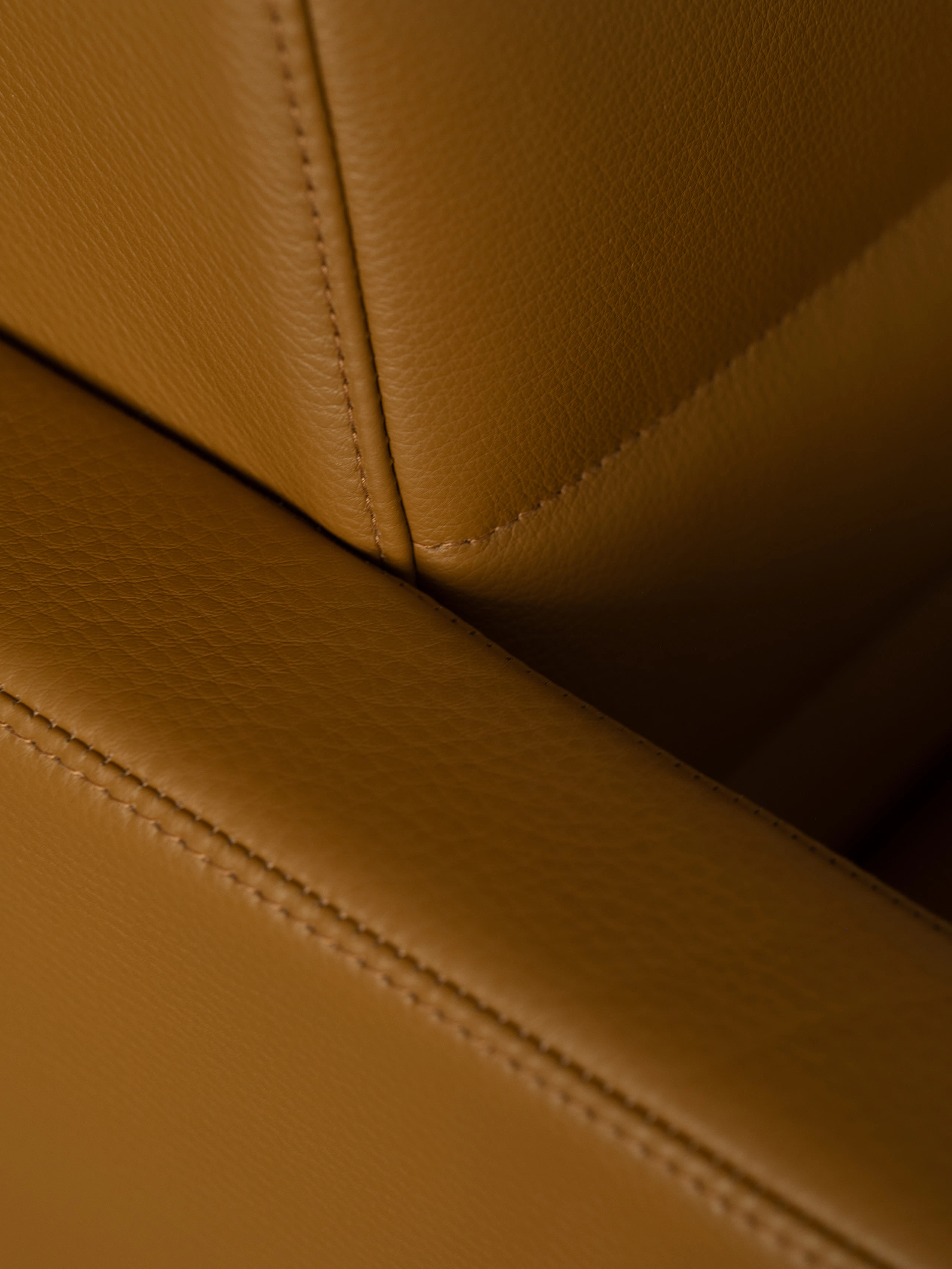 Detail view of a quilted Tuxedo Component Club Chair back and armrest upholstered with Raise Leather in Sienna, viewed at an angle.