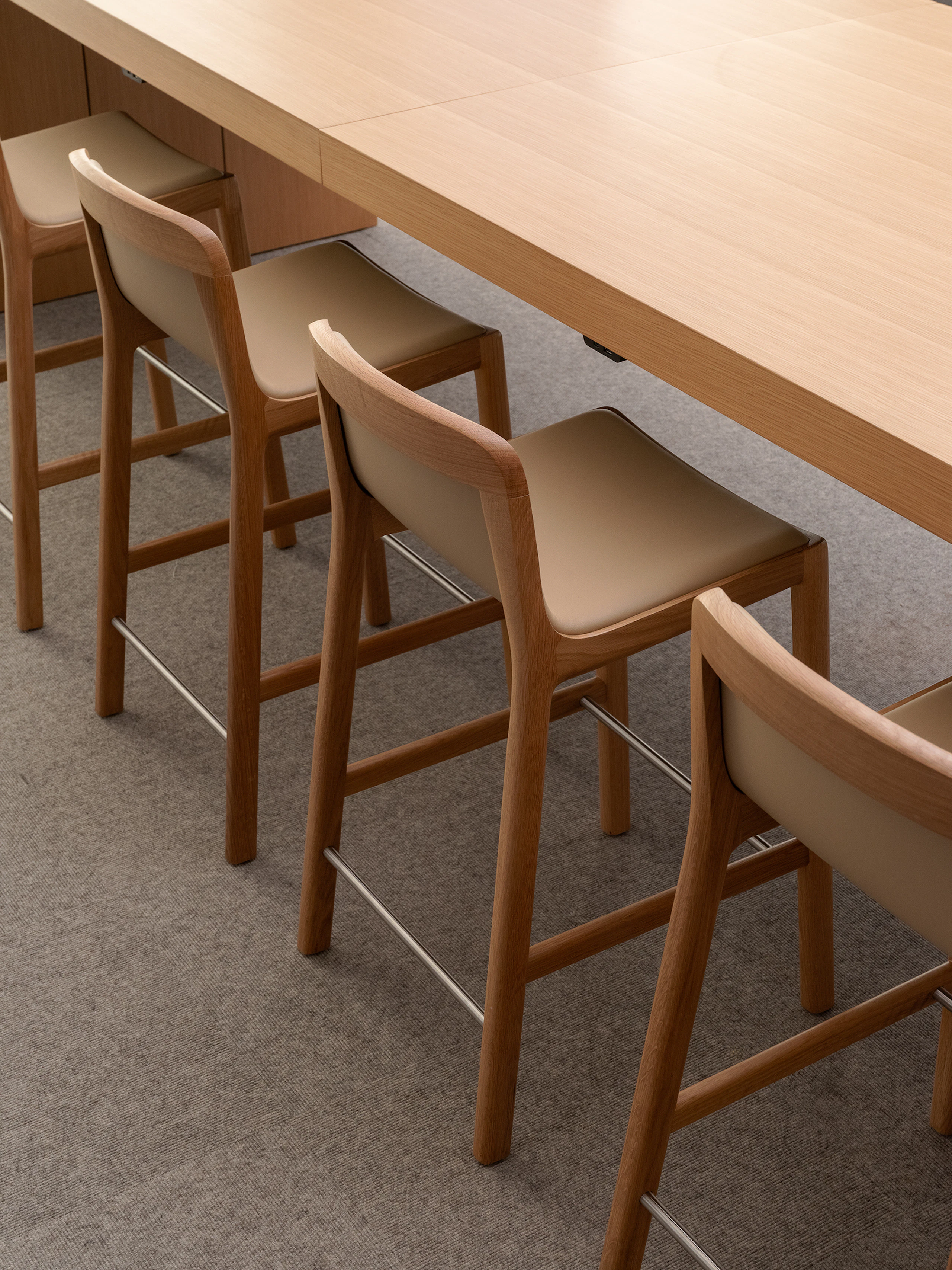 Four counter height Lijn Stools in Natural Oak fully upholstered with Bristol leather in Champagne with a JD Waterfall Table in Natural Rift Cut Oak, viewed from above at an angle.
