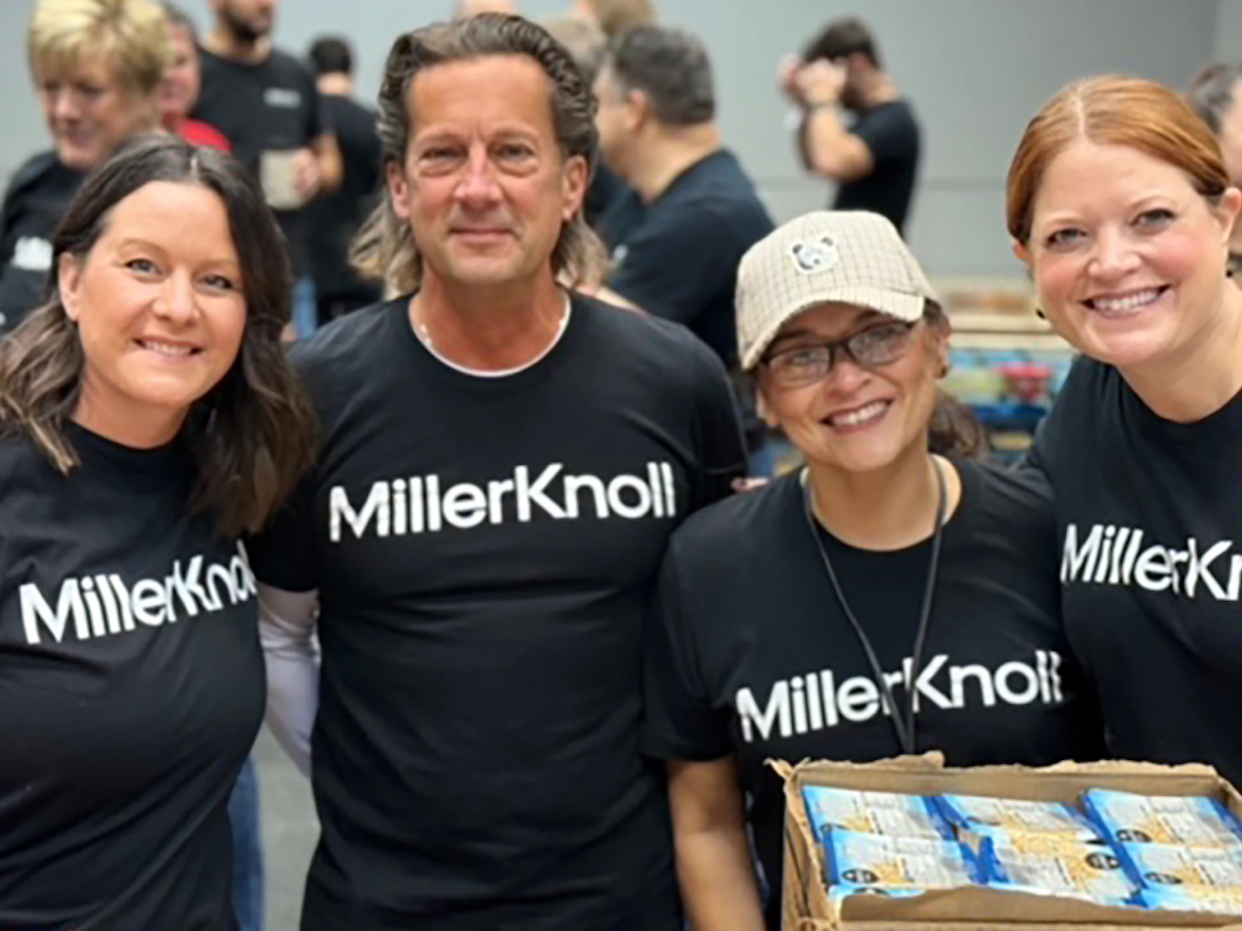 Four smiling MillerKnoll associates wearing black and white MillerKnoll shirts while volunteering at Hand2Hand.