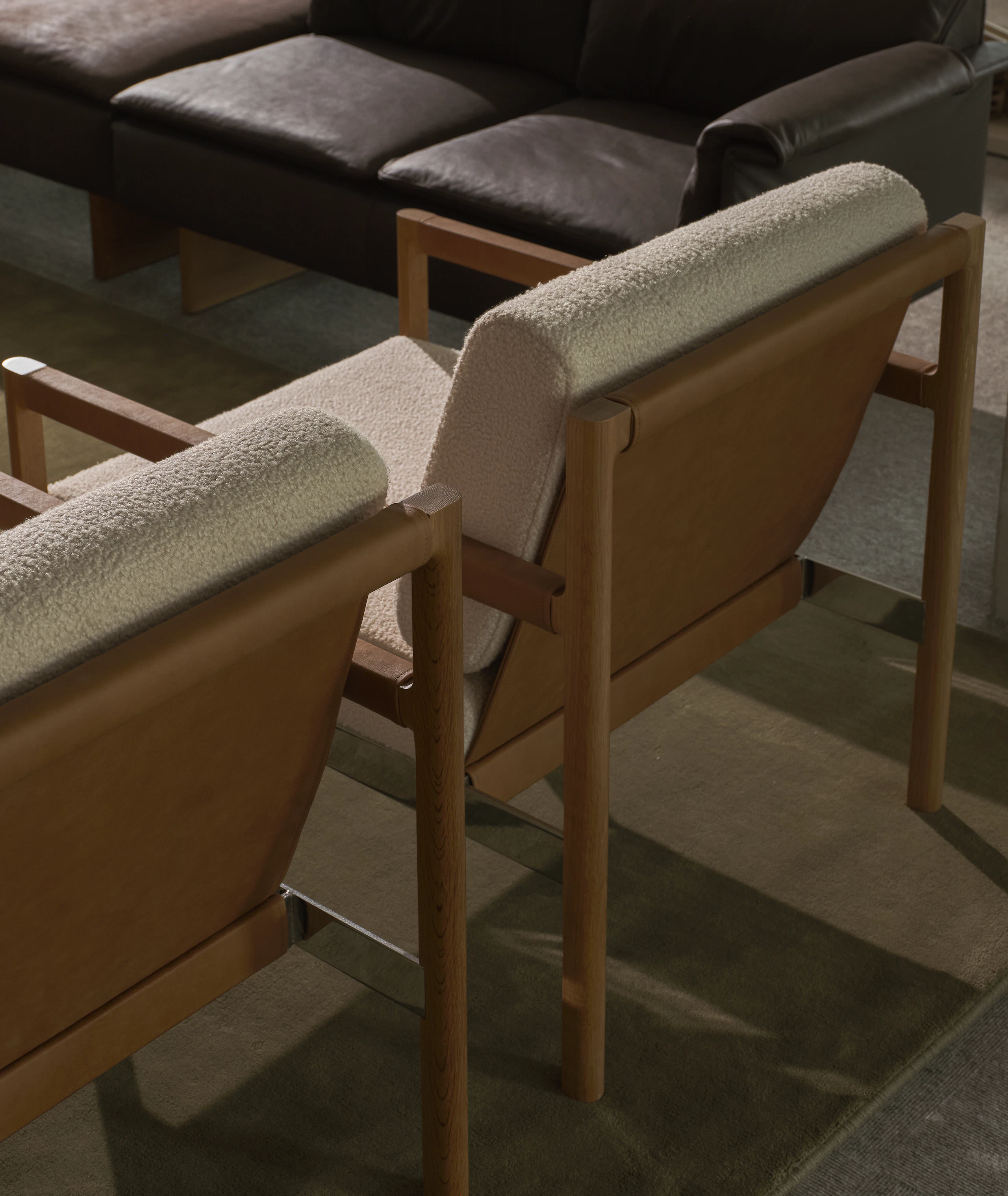 Detail view of the backs of two Brabo Club Chairs with Natural Oak and chrome frames and upholstered with Maharam Firth in Limewash and a Mantle Sectional Sofa in the background, viewed from above at an angle.