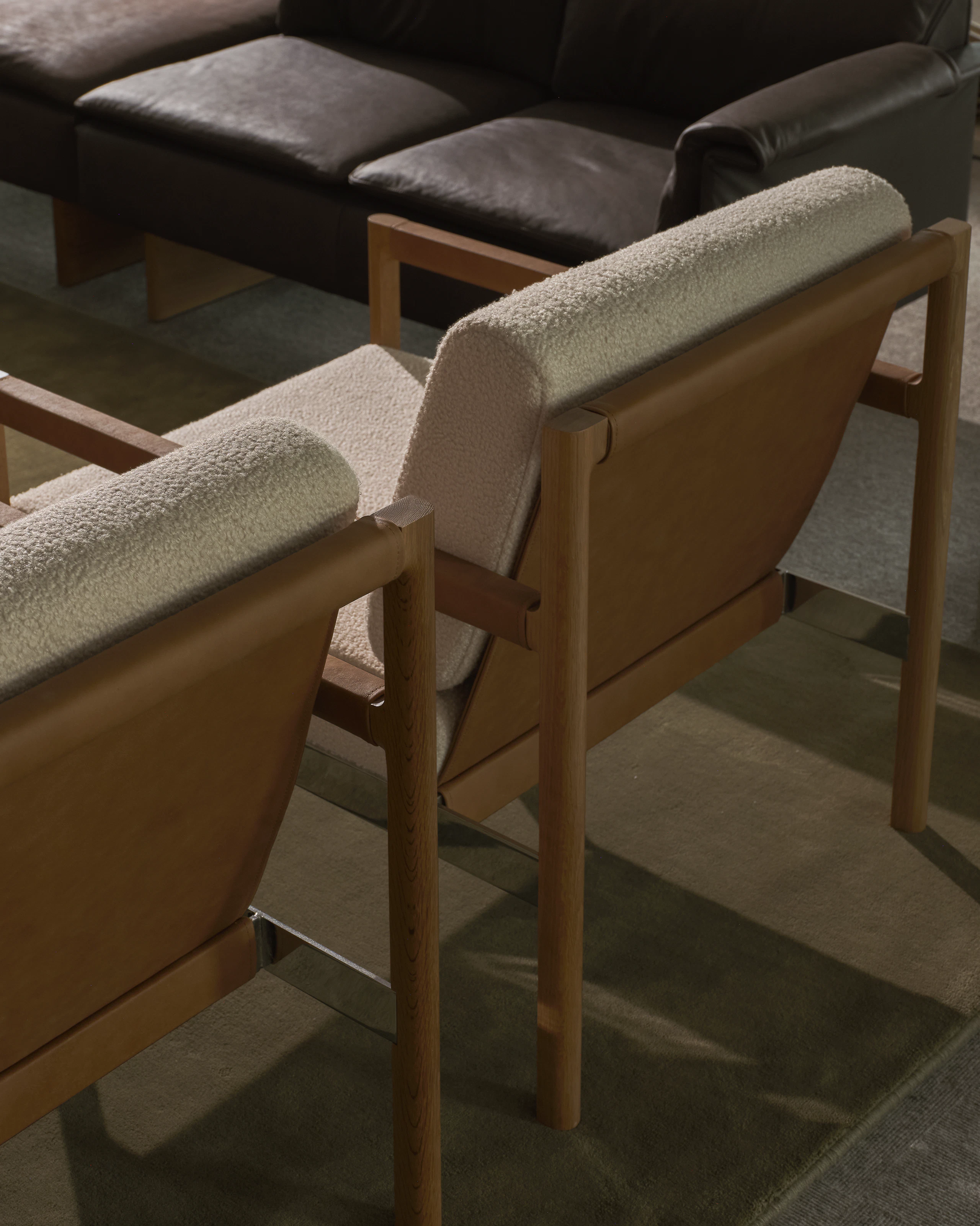 Detail view of the backs of two Brabo Club Chairs with Natural Oak and chrome frames and upholstered with Maharam Firth in Limewash and a Mantle Sectional Sofa in the background, viewed from above at an angle.